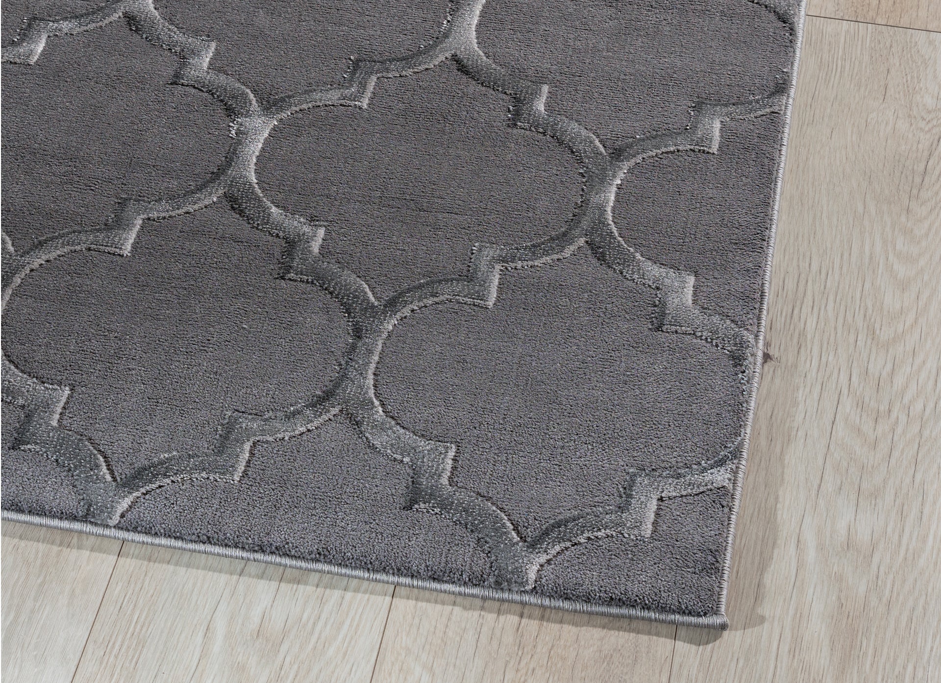 Zbliżenie na róg dywanu Elsher Grey 120x180 cm – widoczne staranne obszycie i miękka faktura runa na tle jasnej podłogi.