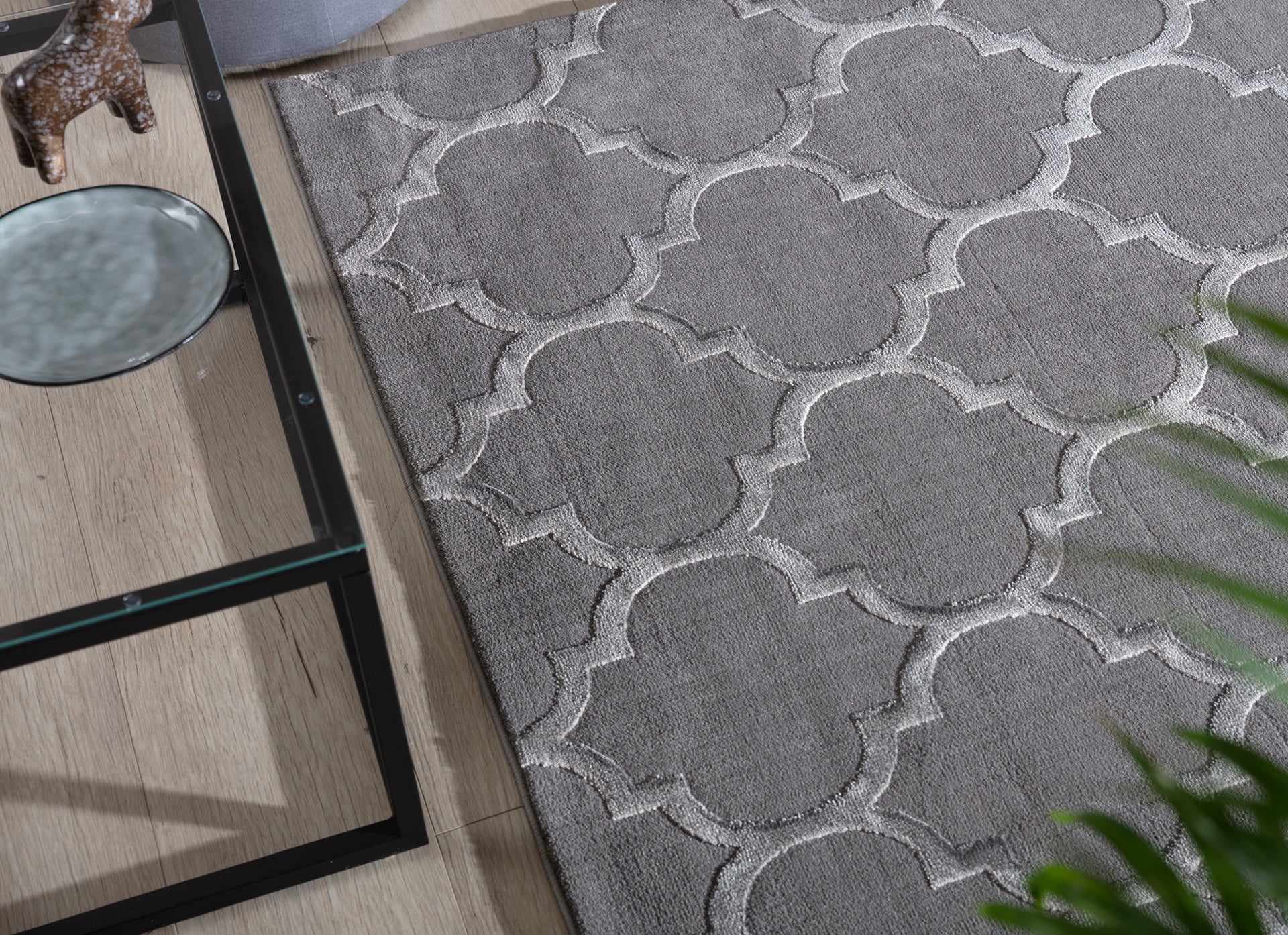 Szary dywan Elsher Grey 80x150 cm z geometrycznym wzorem pod szklaną ławą w nowoczesnym salonie.