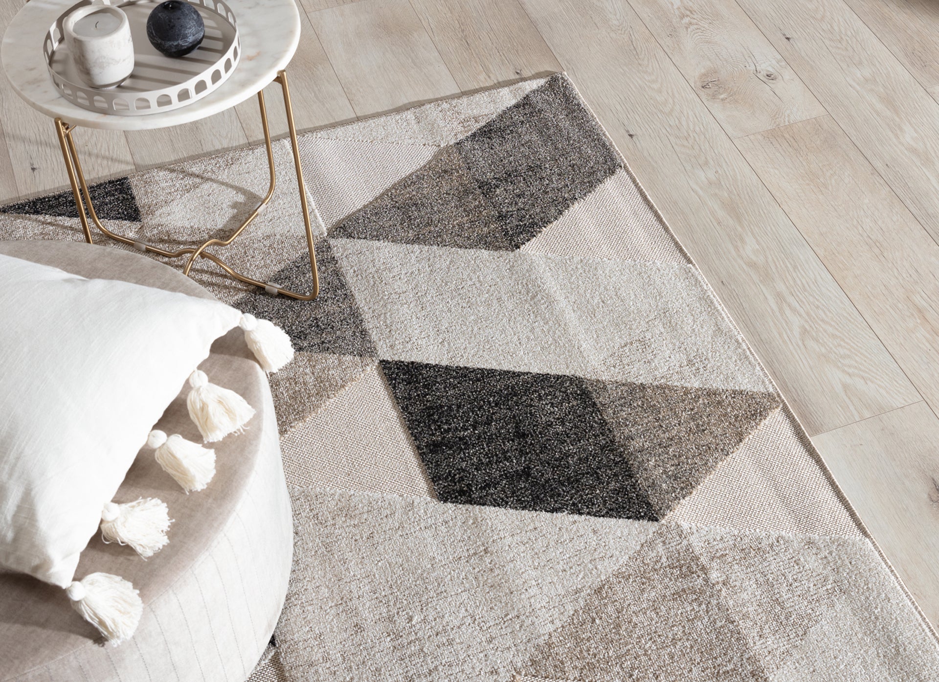 Beżowy dywan Eustache 160x220 cm z geometrycznym wzorem trójkątów ułożony pod stolikiem kawowym z marmurowym blatem i złotymi nogami.