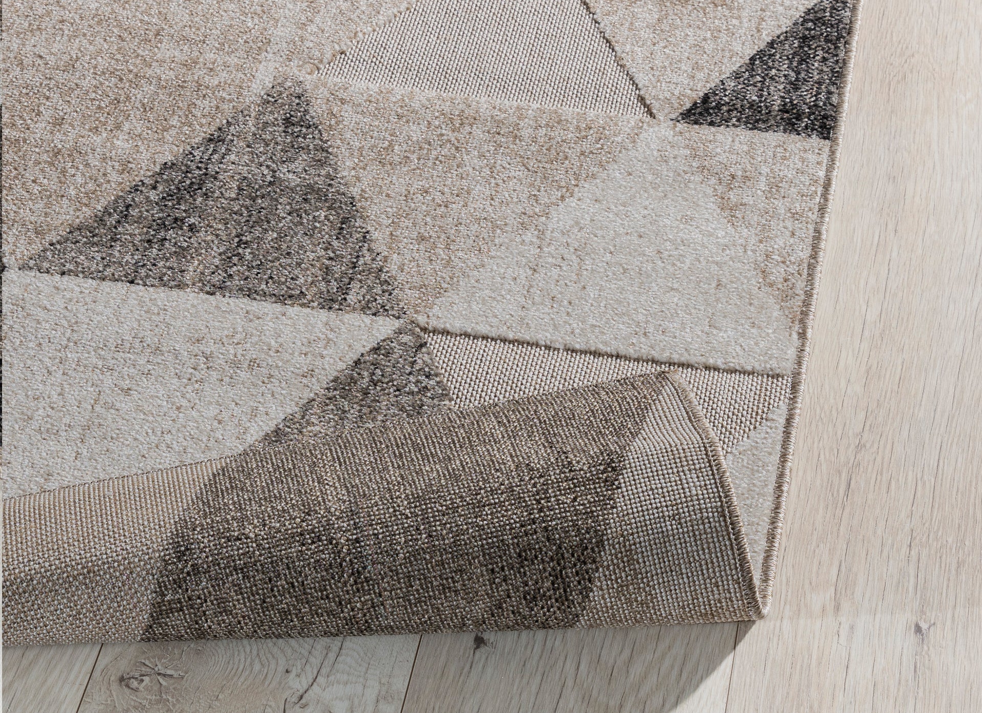Dywan Eustache Beige 160x220 cm z lekko podwiniętą krawędzią – widoczna struktura materiału i solidne wykonanie spodniej warstwy.