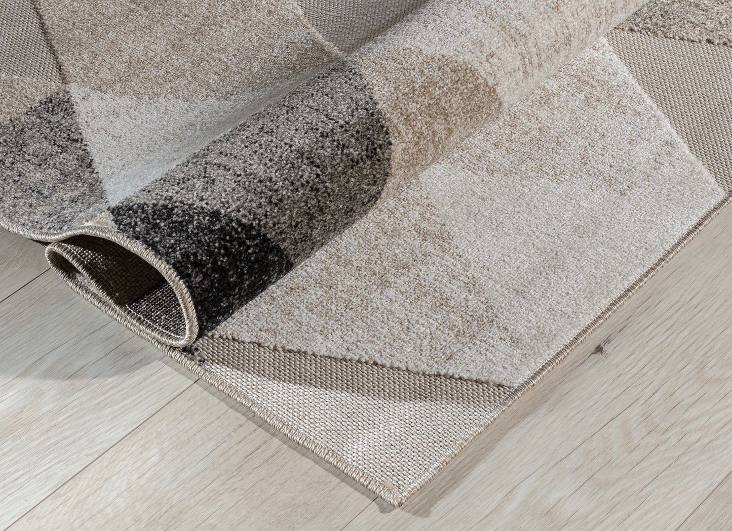 Dywan Eustache Beige 160x220 cm zwinięty w rulon – prezentacja grubości, faktury i geometrycznego wzoru w neutralnych barwach.