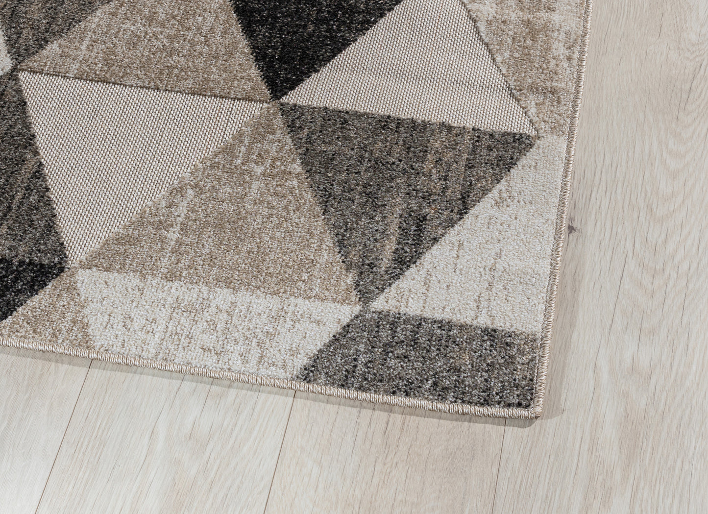 Zbliżenie na róg dywanu Eustache Beige 80x150 cm – widoczne staranne obszycie i struktura materiału na tle drewnianej podłogi.