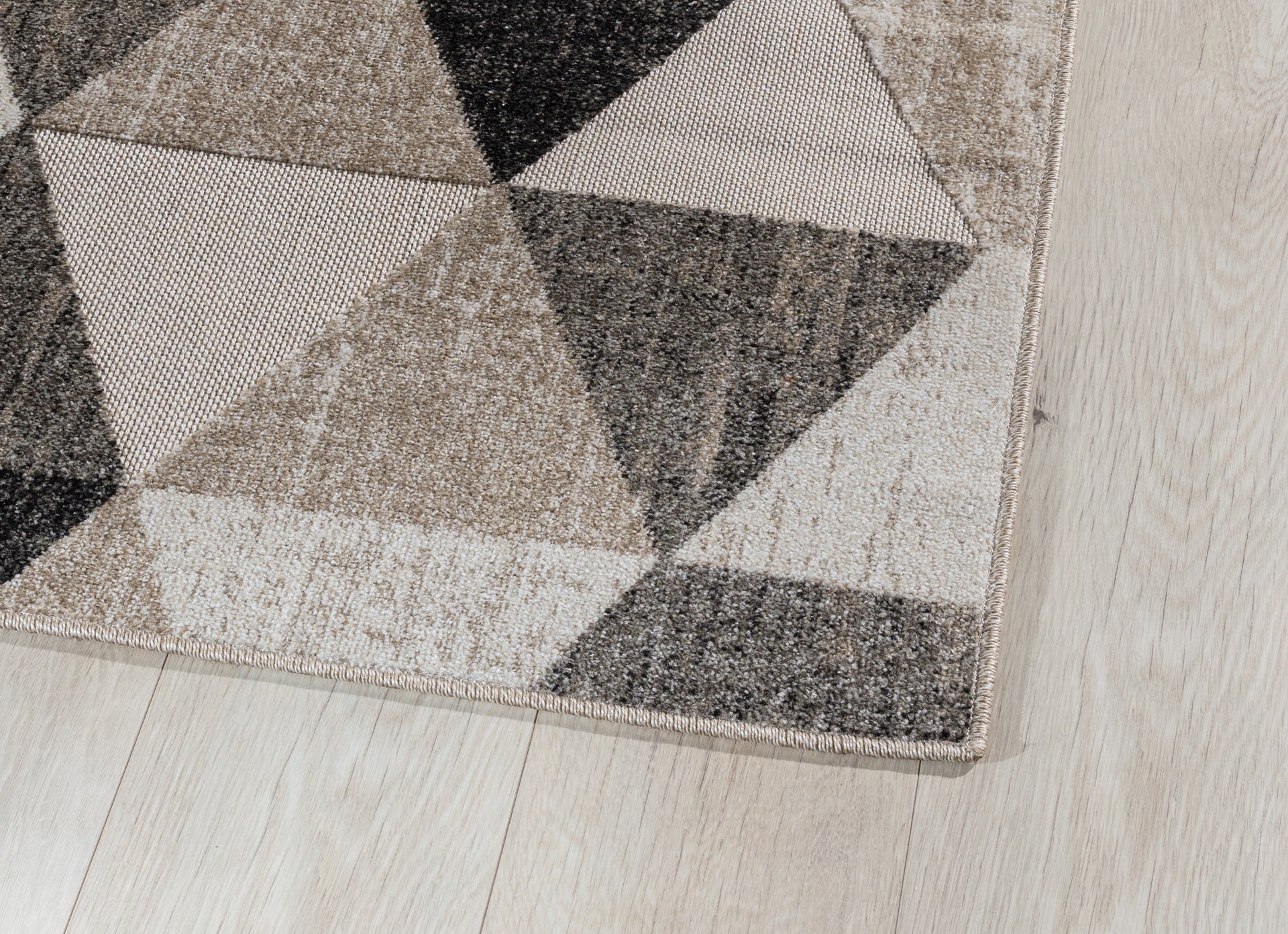 Zbliżenie na róg dywanu Eustache Beige 80x150 cm – widoczne staranne obszycie i struktura materiału na tle drewnianej podłogi.