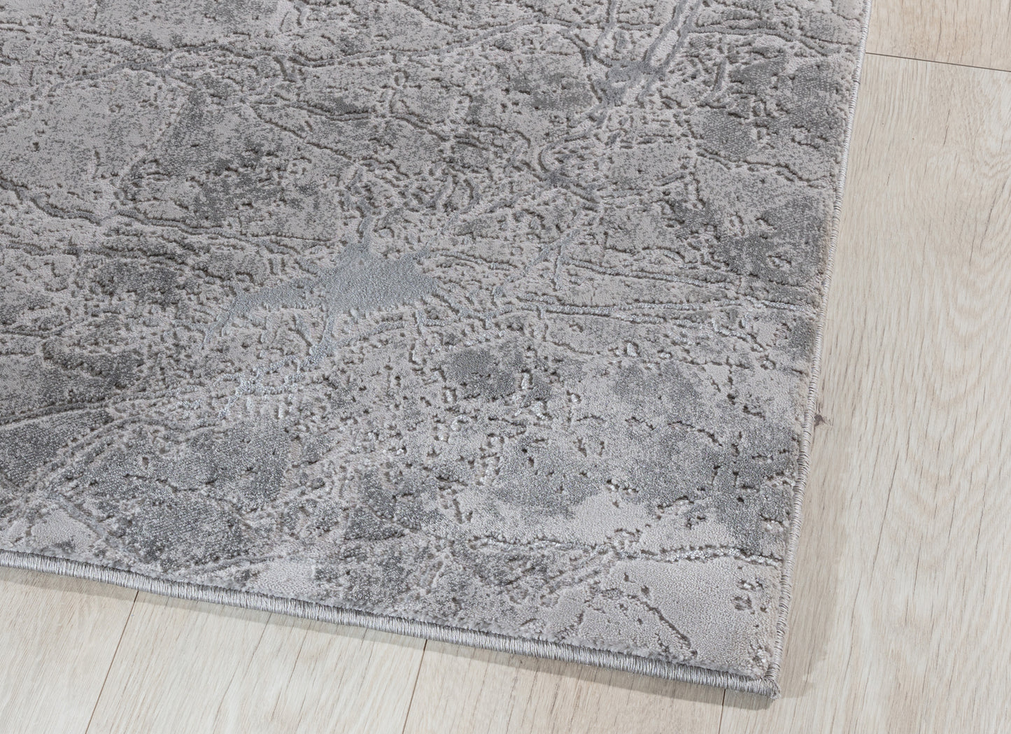 Zbliżenie na róg dywanu Siggi Grey 120x180 cm – widoczne staranne obszycie i faktura runa w odcieniach szarości.