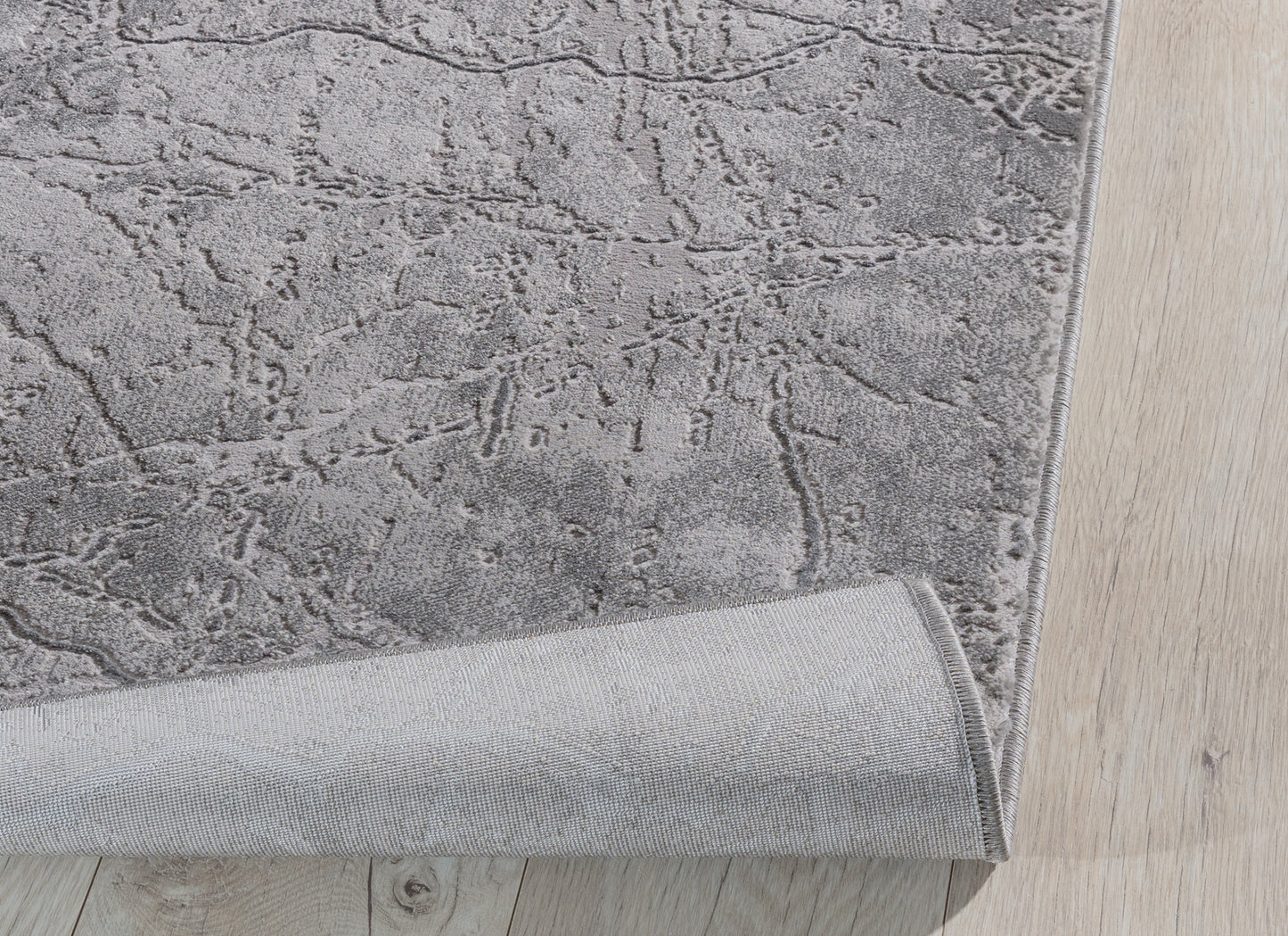 Dywan Siggi Grey 120x180 cm z lekko podwiniętą krawędzią – prezentacja elastyczności i spodniej warstwy tkaniny.