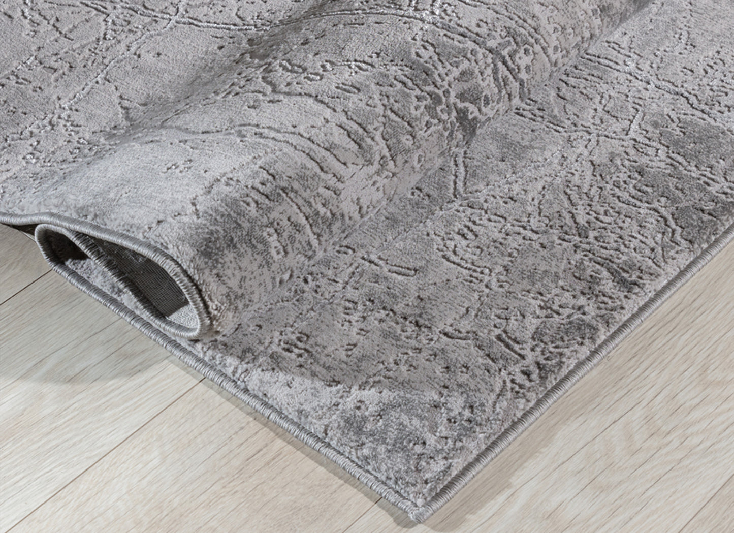 Dywan Siggi Grey 120x180 cm zwinięty w rulon – widoczna miękka powierzchnia i nieregularny wzór w szarej kolorystyce.