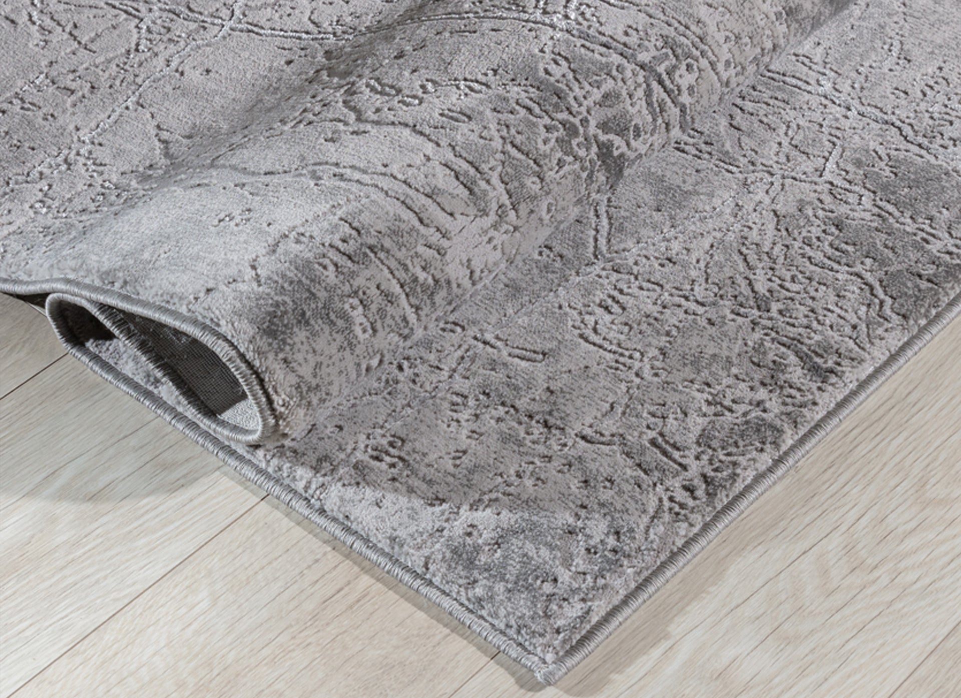 Dywan Siggi Grey 160x220 cm zwinięty w rulon – widoczna grubość, struktura i nieregularny wzór w różnych odcieniach szarości.