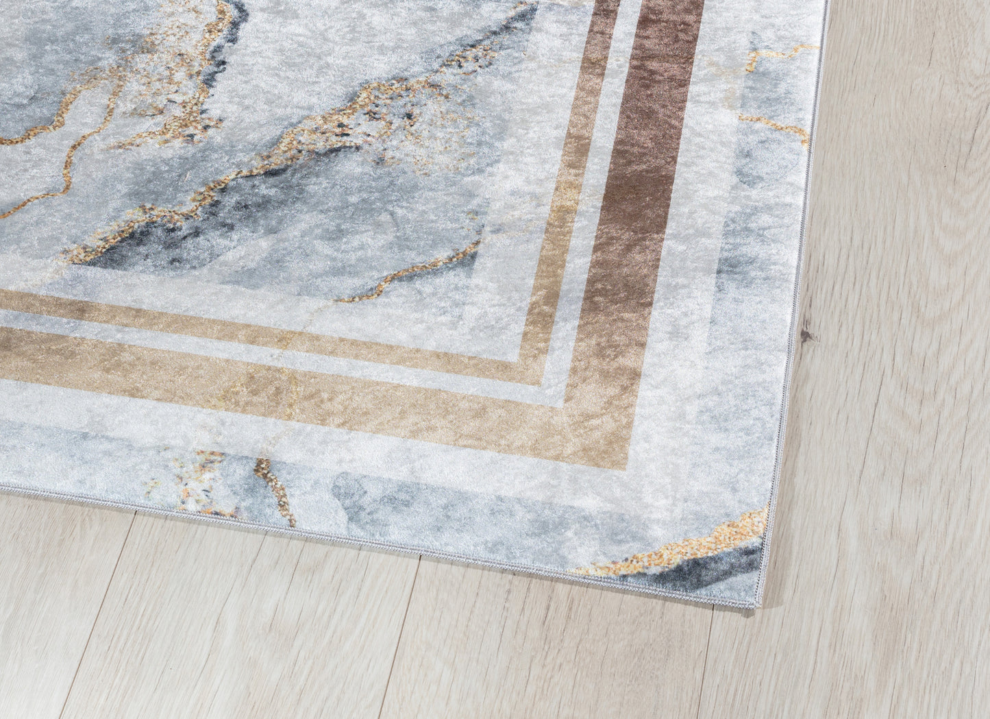 Zbliżenie na róg dywanu Squitta Grey 120x180 cm – widoczne złote akcenty, precyzyjne obszycie i miękka powierzchnia.