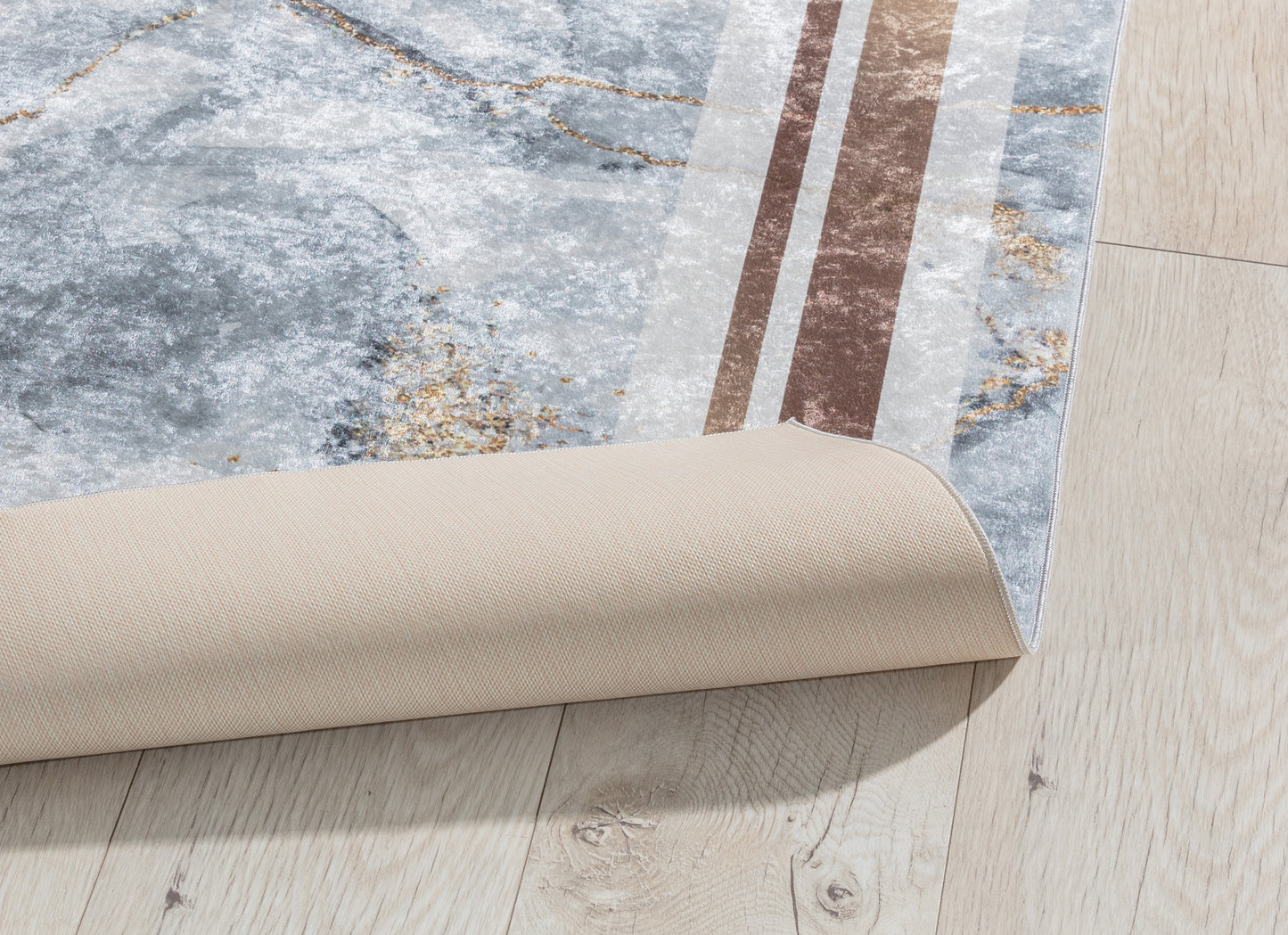 Dywan Squitta Grey 120x180 cm z lekko podwiniętą krawędzią – prezentacja spodniej warstwy i elastycznej struktury tkaniny.