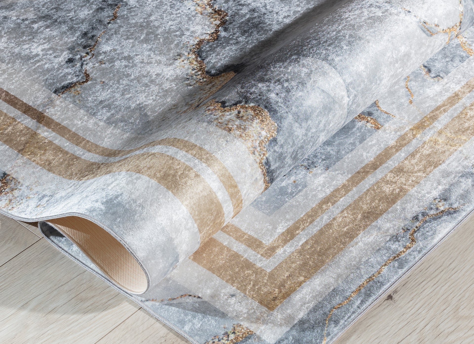 Dywan Squitta Grey 120x180 cm zwinięty w rulon – widoczny marmurowy wzór z połyskującymi złotymi liniami.