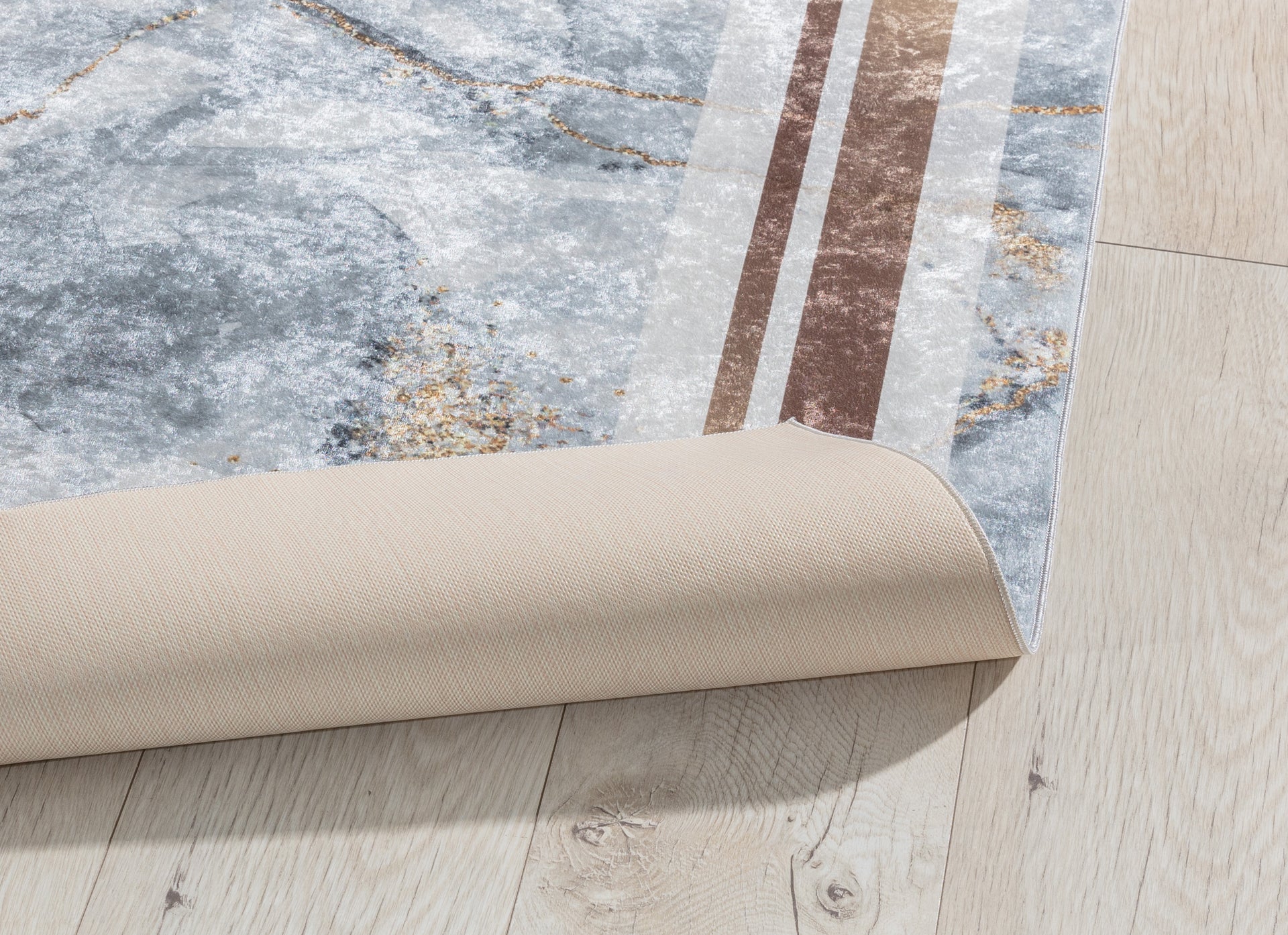 Dywan Squitta Grey 160x220 cm z lekko podwiniętą krawędzią – pokazany spód w beżowym kolorze i elastyczna struktura materiału.