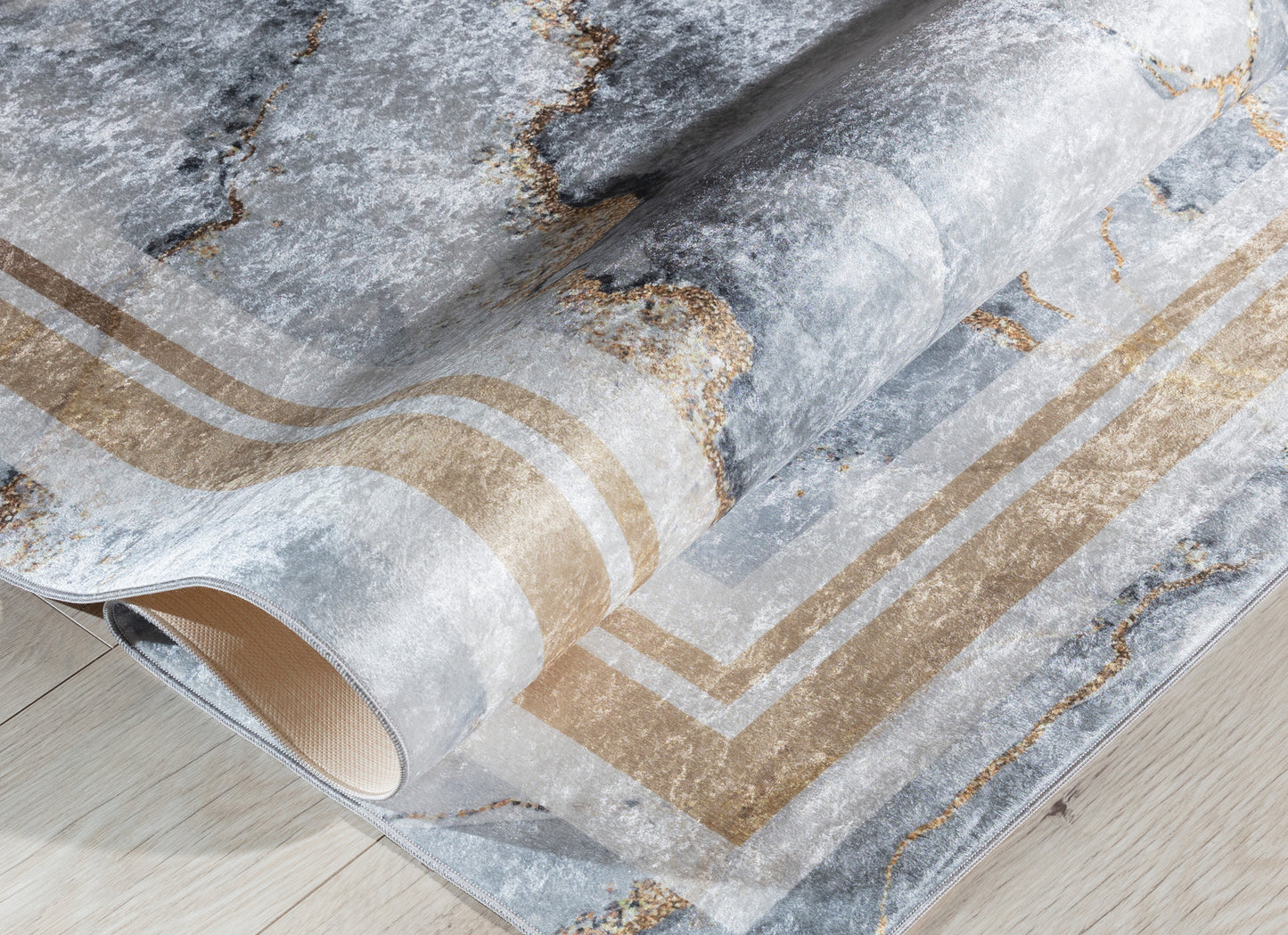 Dywan Squitta Grey 80x150 cm zwinięty w rulon – widoczny marmurowy wzór i błyszczące złote detale.
