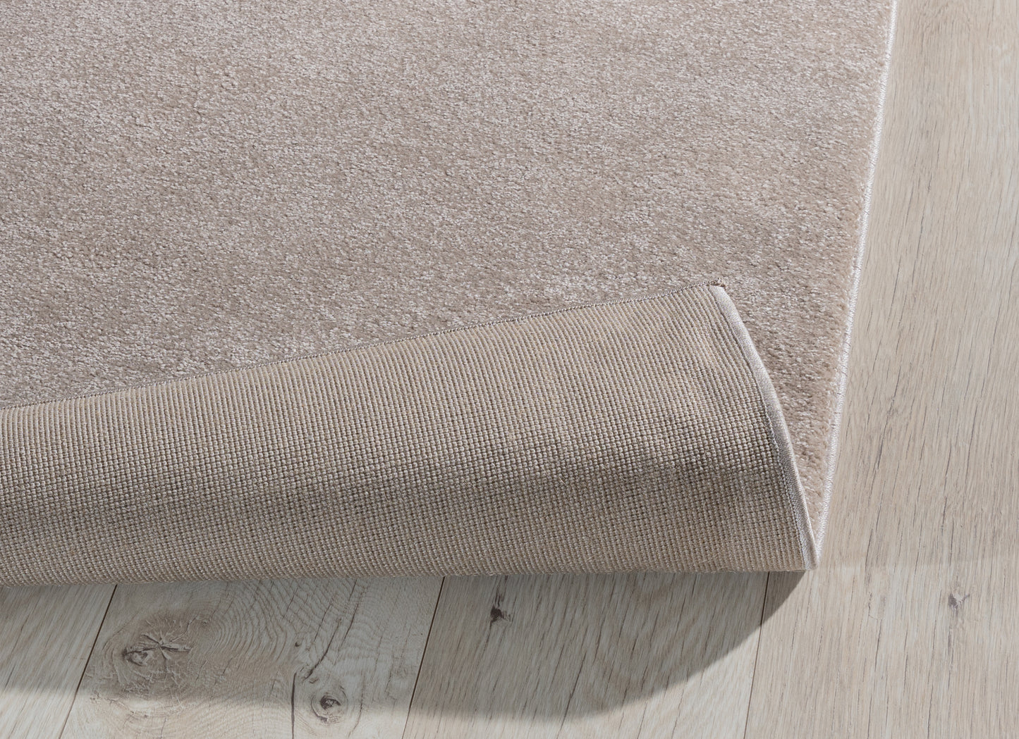 Dywan Verlice Beige 160x230 cm z lekko podwiniętą krawędzią – pokazany beżowy spód o antypoślizgowej strukturze.