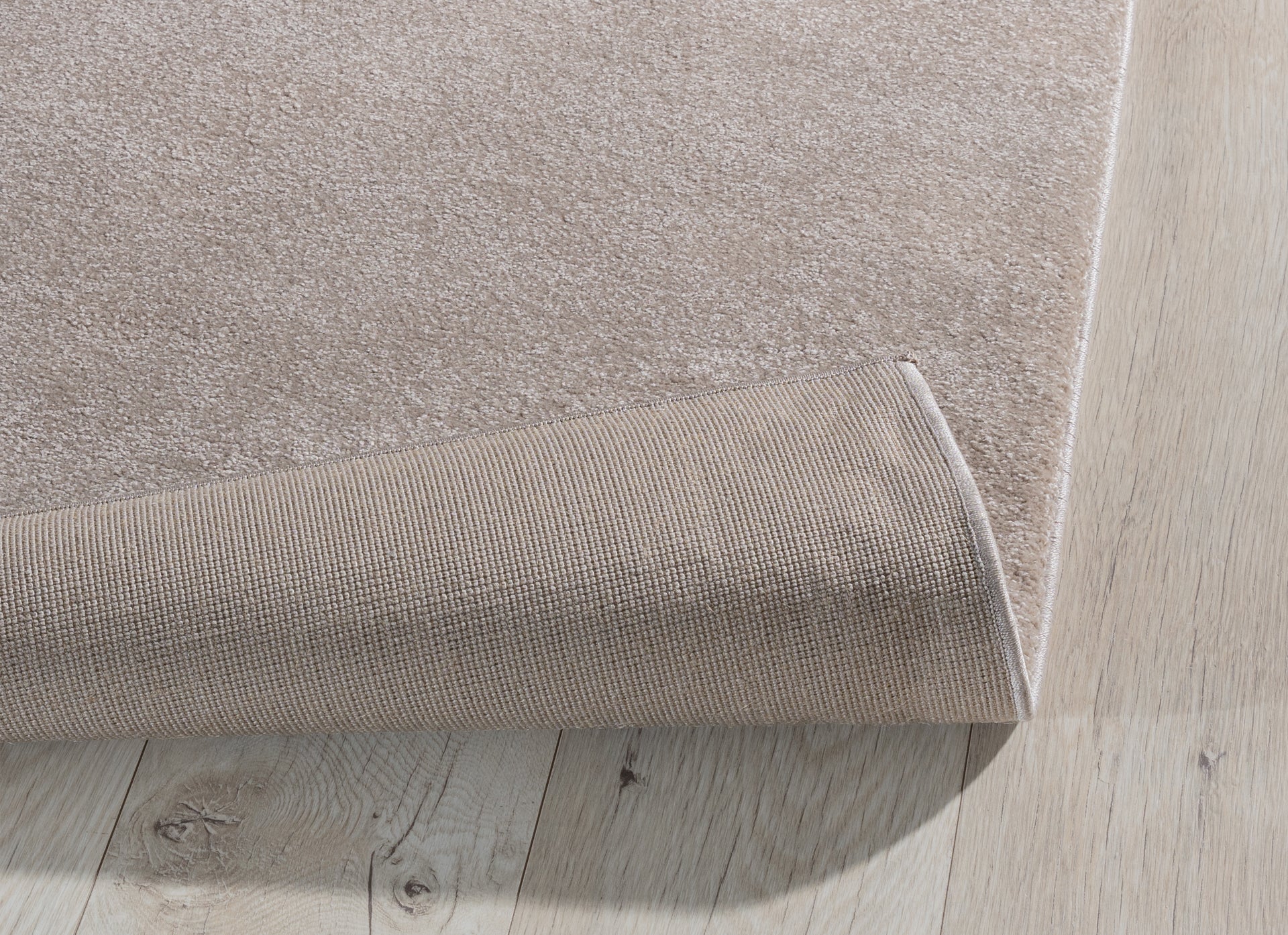 Dywan Verlice Beige 160x230 cm z lekko podwiniętą krawędzią – pokazany beżowy spód o antypoślizgowej strukturze.