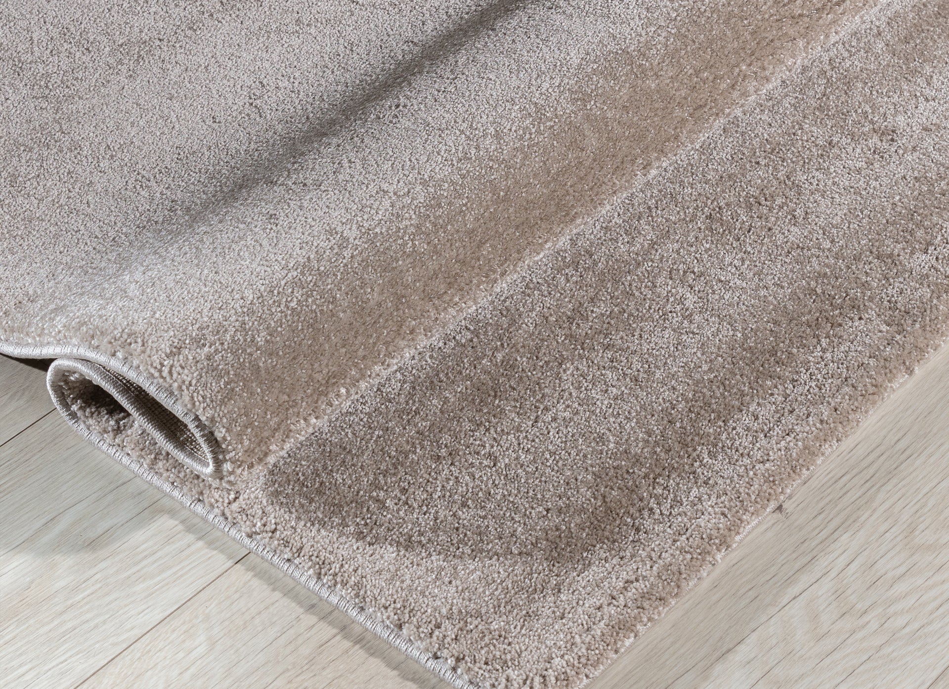 Dywan Verlice Beige 80x150 cm częściowo zwinięty – prezentacja grubości runa i miękkiej, welurowej faktury.