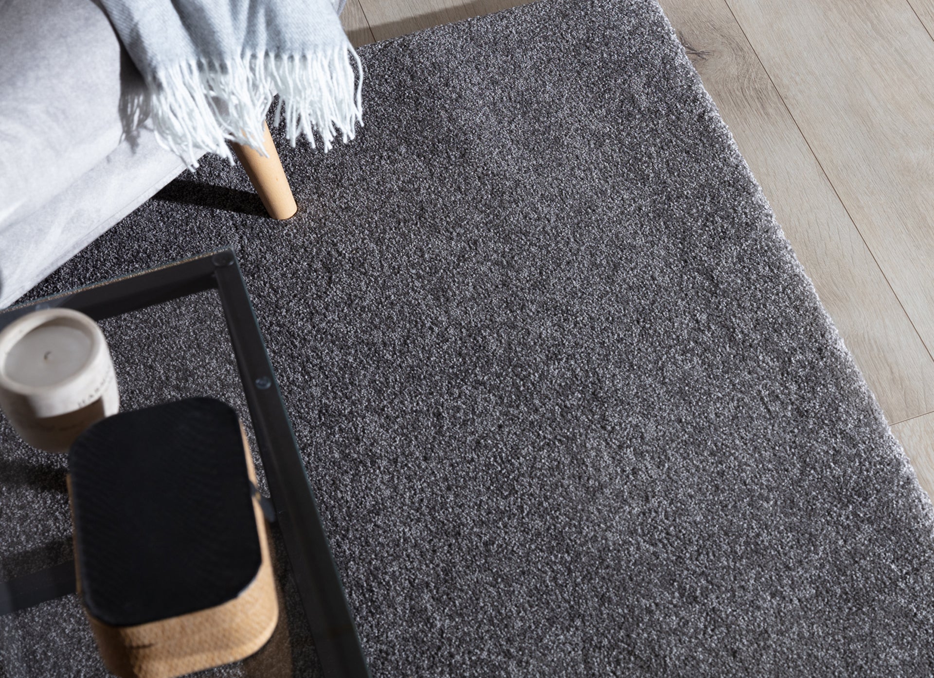 Szary dywan Verlice 160x230 cm ułożony przy sofie z kocem i stolikiem kawowym – widoczne delikatne runo i eleganckie wykończenie