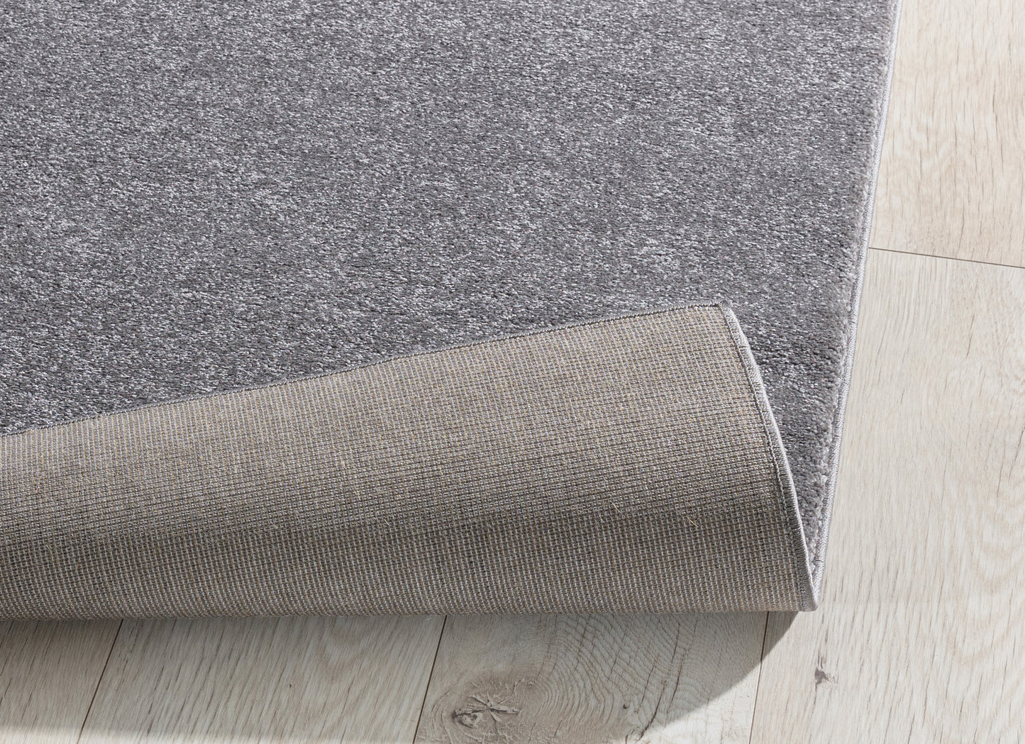 Dywan Verlice Grey 160x230 cm częściowo zwinięty – widoczna grubość runa i puszysta struktura materiału.