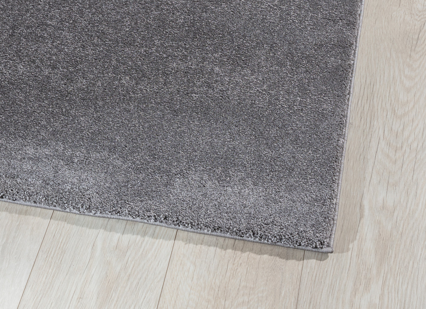 Zbliżenie na róg dywanu Verlice Grey 80x150 cm – gęste włókna i precyzyjnie obszyta krawędź na tle jasnej podłogi.