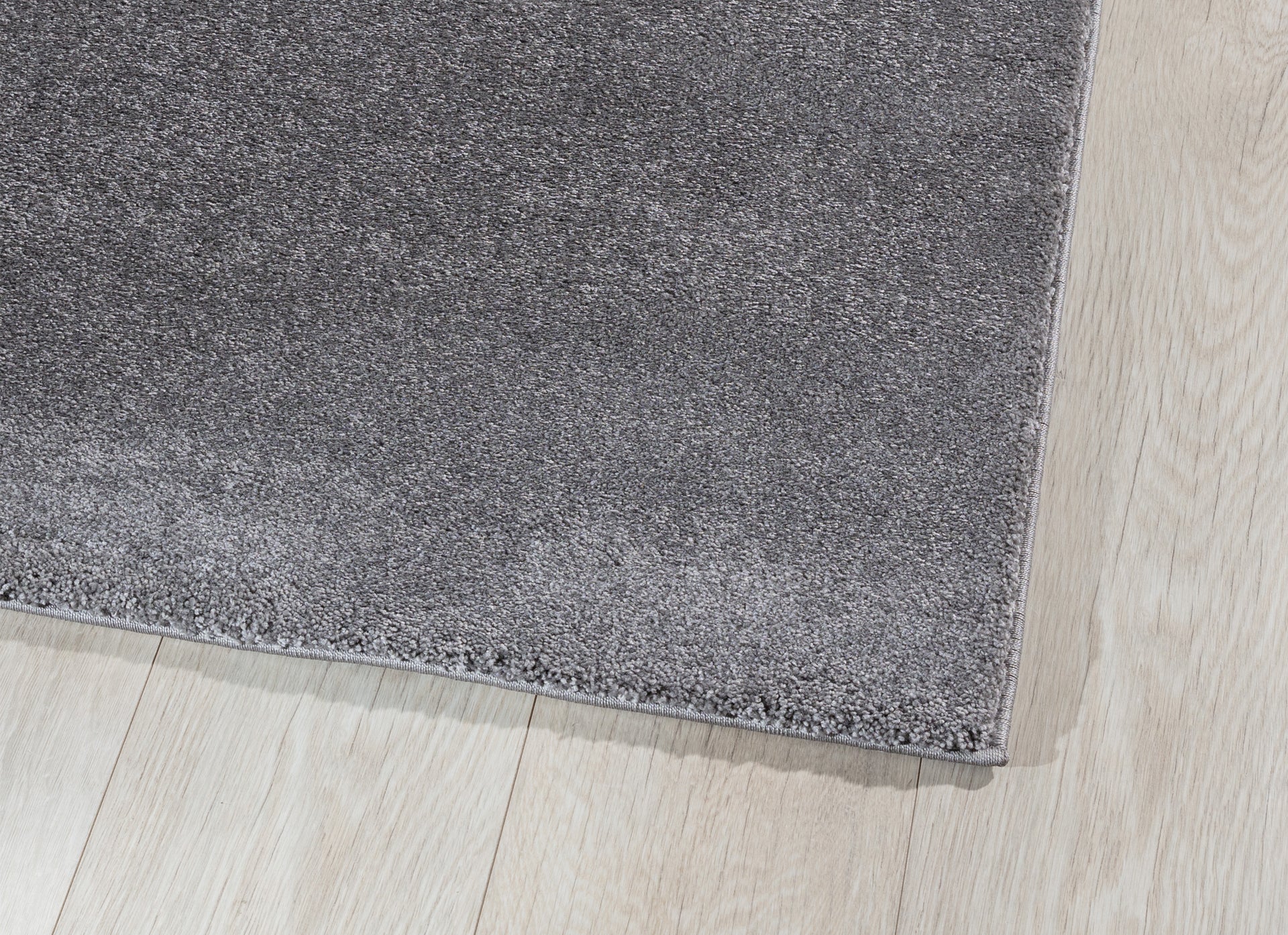 Zbliżenie na róg dywanu Verlice Grey 80x150 cm – gęste włókna i precyzyjnie obszyta krawędź na tle jasnej podłogi.