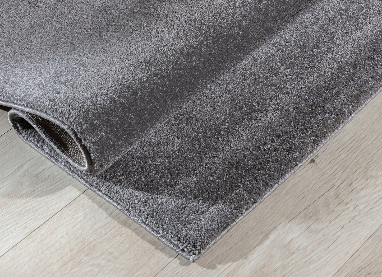 Dywan Verlice Grey 80x150 cm częściowo zwinięty – widoczna grubość i miękka, puszysta powierzchnia.