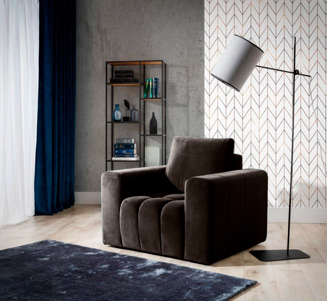 Fotel Lazaro w kolorze Monolith 29 brązowy w eleganckim salonie z niebieskimi zasłonami, wzorzystą tapetą i czarną lampą stojącą, ustawiony przy regale z dekoracjami i książkami.