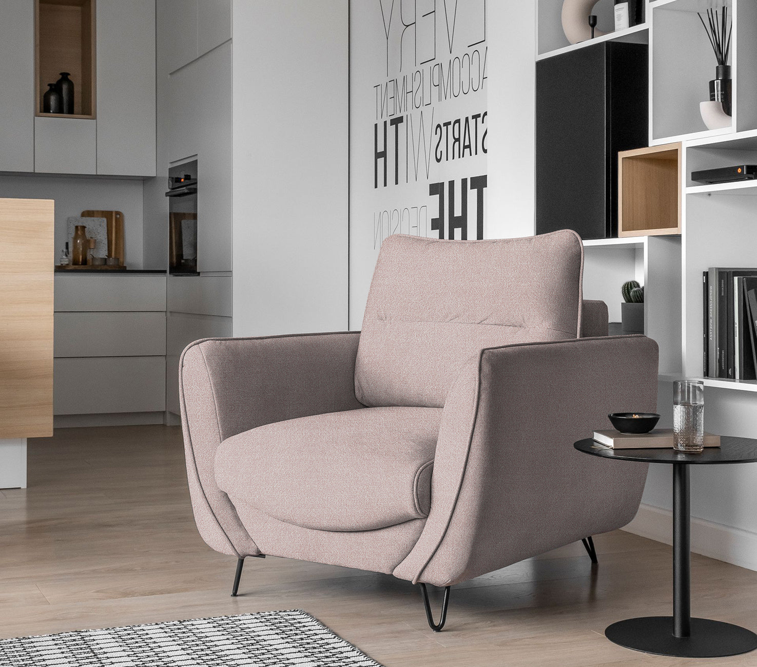 Fotel Silva w kolorze Gojo 101 jasnoróżowy w eleganckim salonie, ustawiony przy stoliku kawowym i regale w jasnym, minimalistycznym wnętrzu.