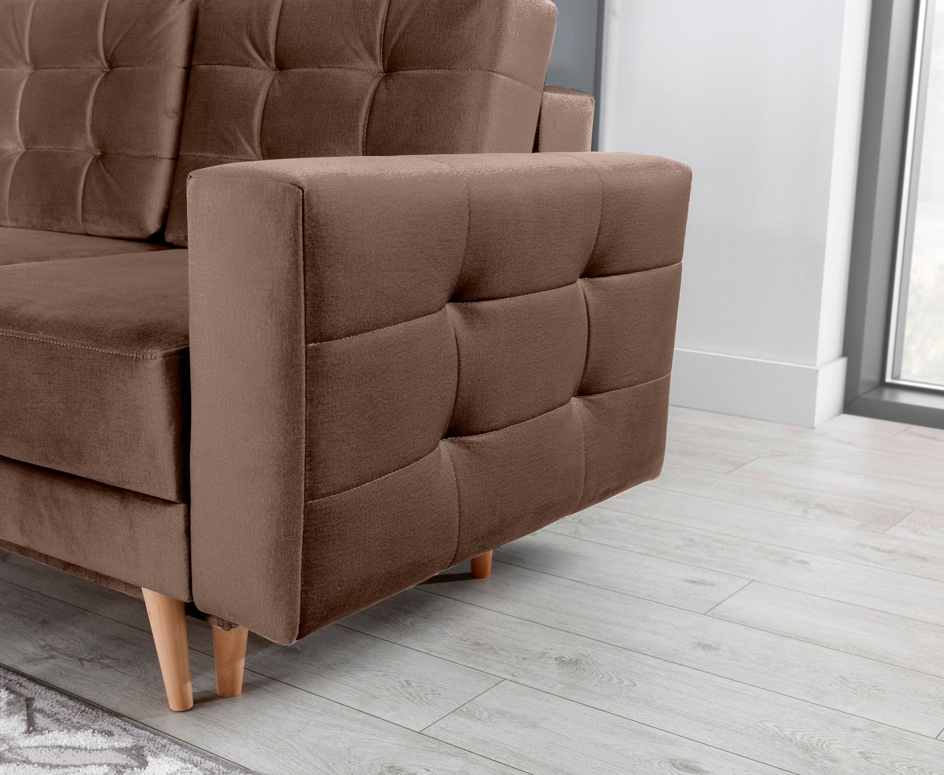 Zbliżenie na podłokietnik i tapicerkę kanapy Asgard w tkaninach Monolith 09 i Monolith 29 – detal pikowanego wykończenia i drewnianych nóg.