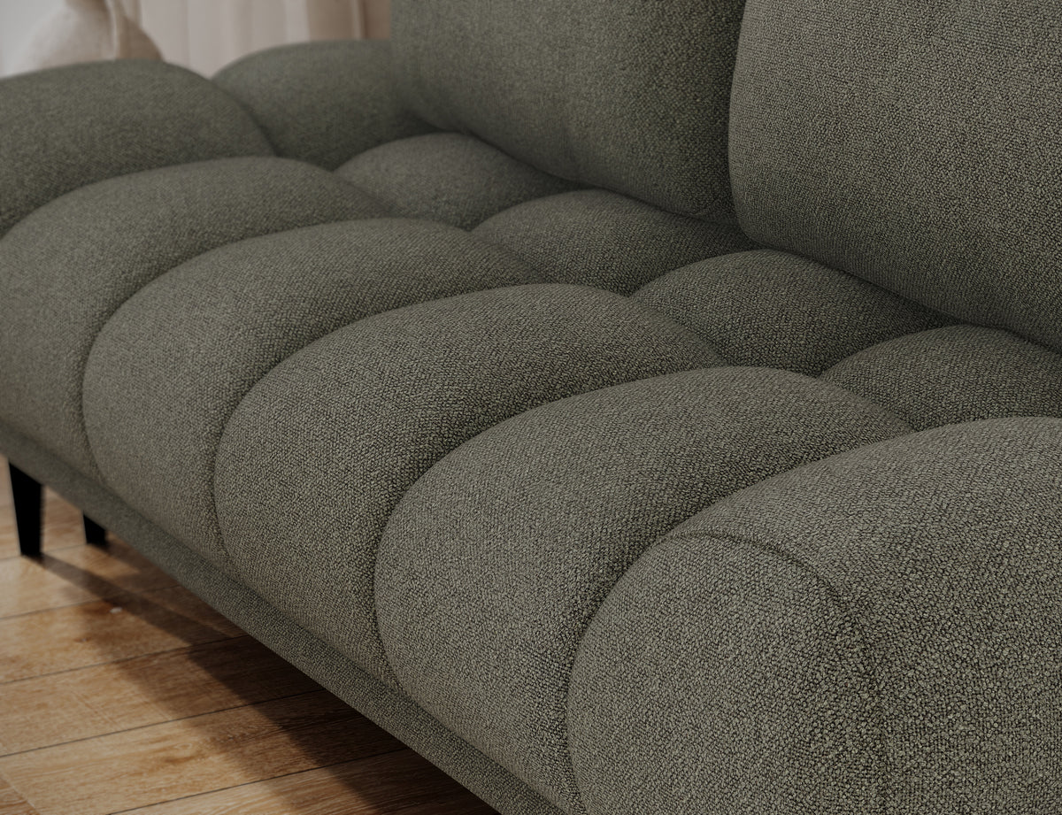 Jasnozielona kanapa Guavio, zbliżenie na segmentowe, zaokrąglone siedzisko z przeszyciami oraz dolną część dwóch poduszek oparcia