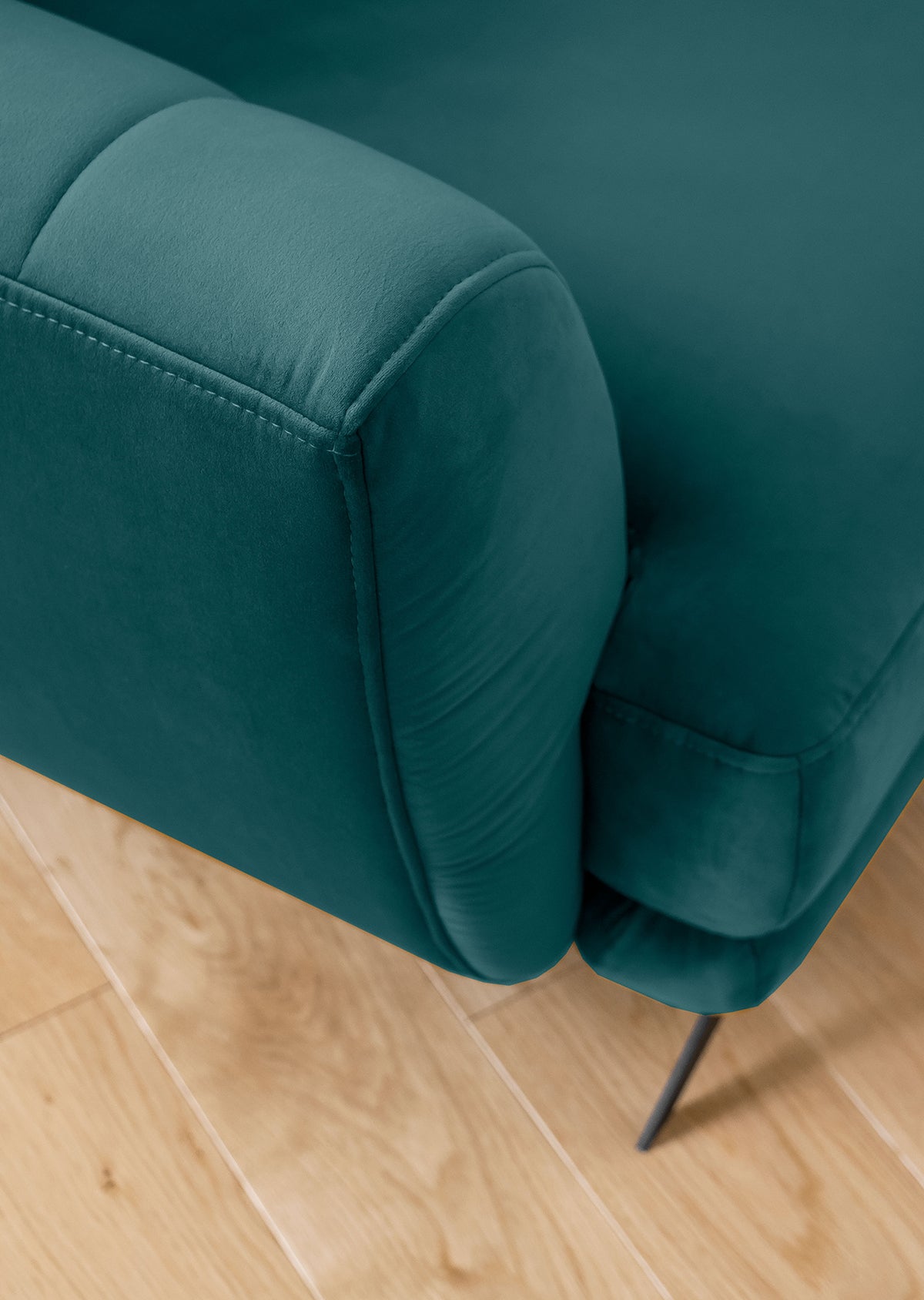 Fragment sofy Megis Velvetmat w kolorze zielonym z czarną, smukłą nóżką. Widoczna struktura tkaniny podkreśla elegancki charakter kompletu.
