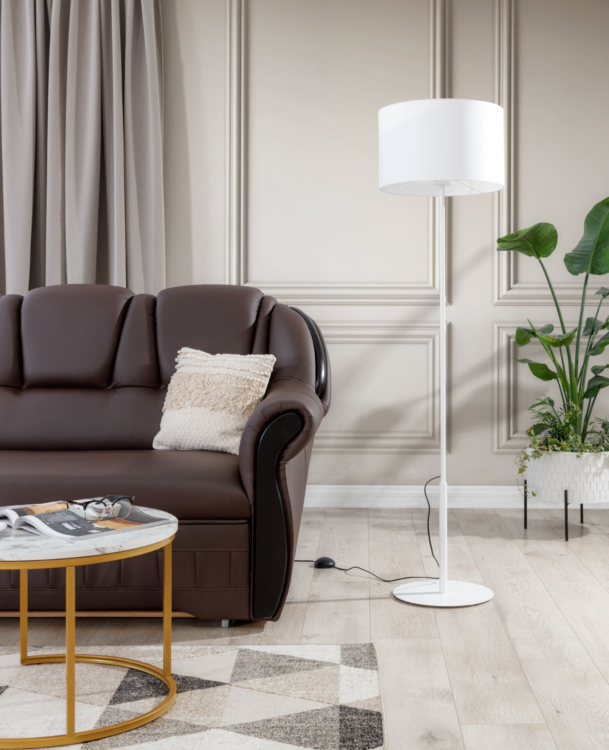 Biała lampa stojąca Vespillo ustawiona obok brązowej sofy i stolika kawowego w eleganckim salonie z dekoracyjnymi panelami ściennymi.