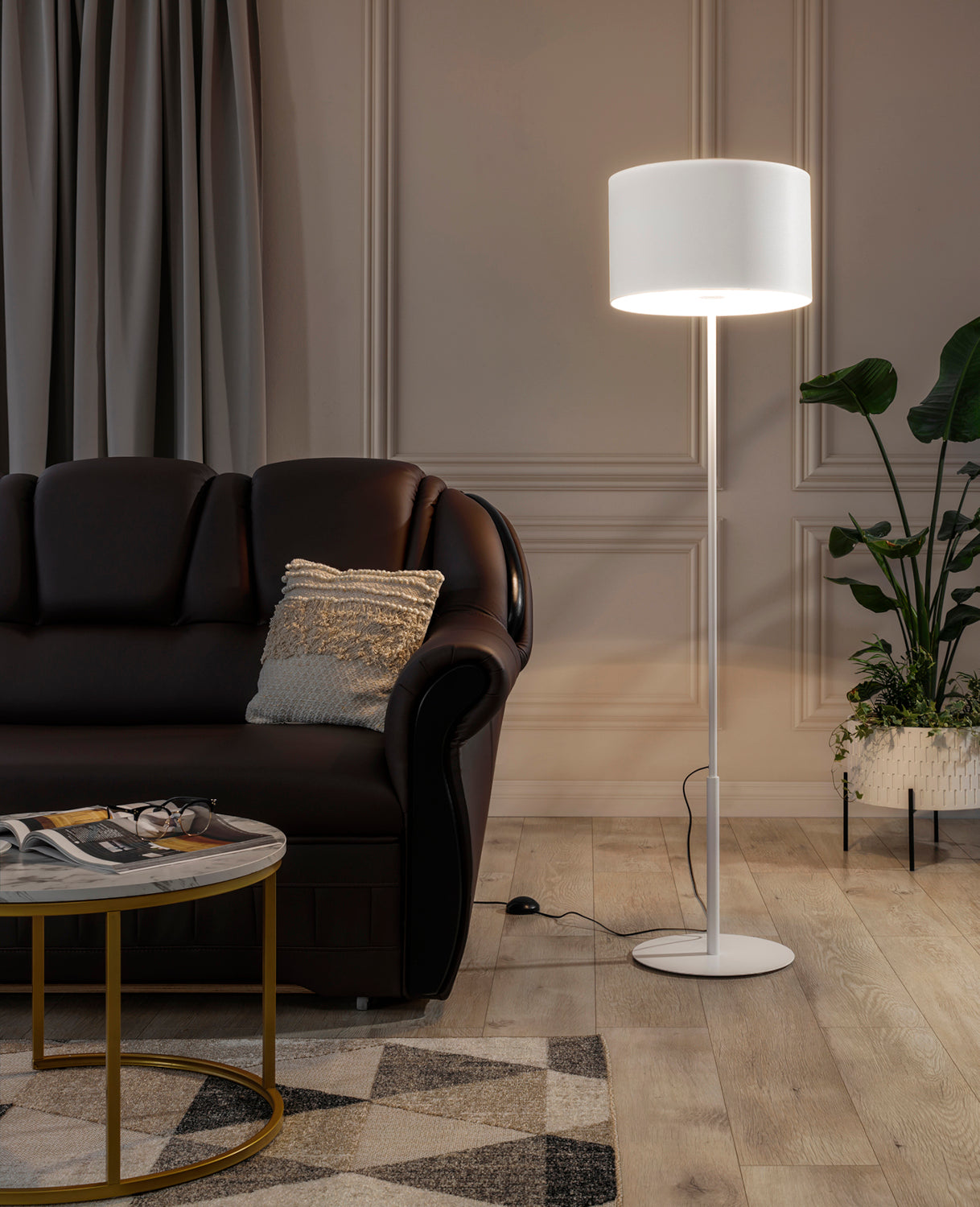 Włączona biała lampa stojąca Vespillo obok eleganckiej sofy i rośliny doniczkowej, rzucająca miękkie, ciepłe światło na salonową aranżację.