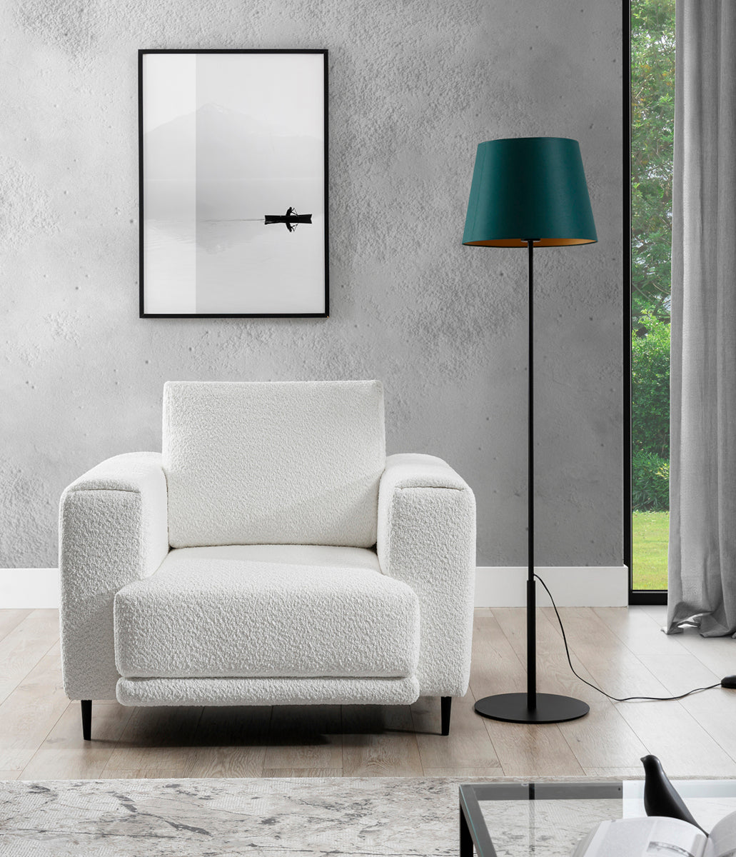 Lampa Vespillo 1a ustawiona obok białego fotela w nowoczesnym salonie z betonową ścianą, dużym oknem i grafiką w czarnej ramie, tworzy skupiony kąt do czytania.