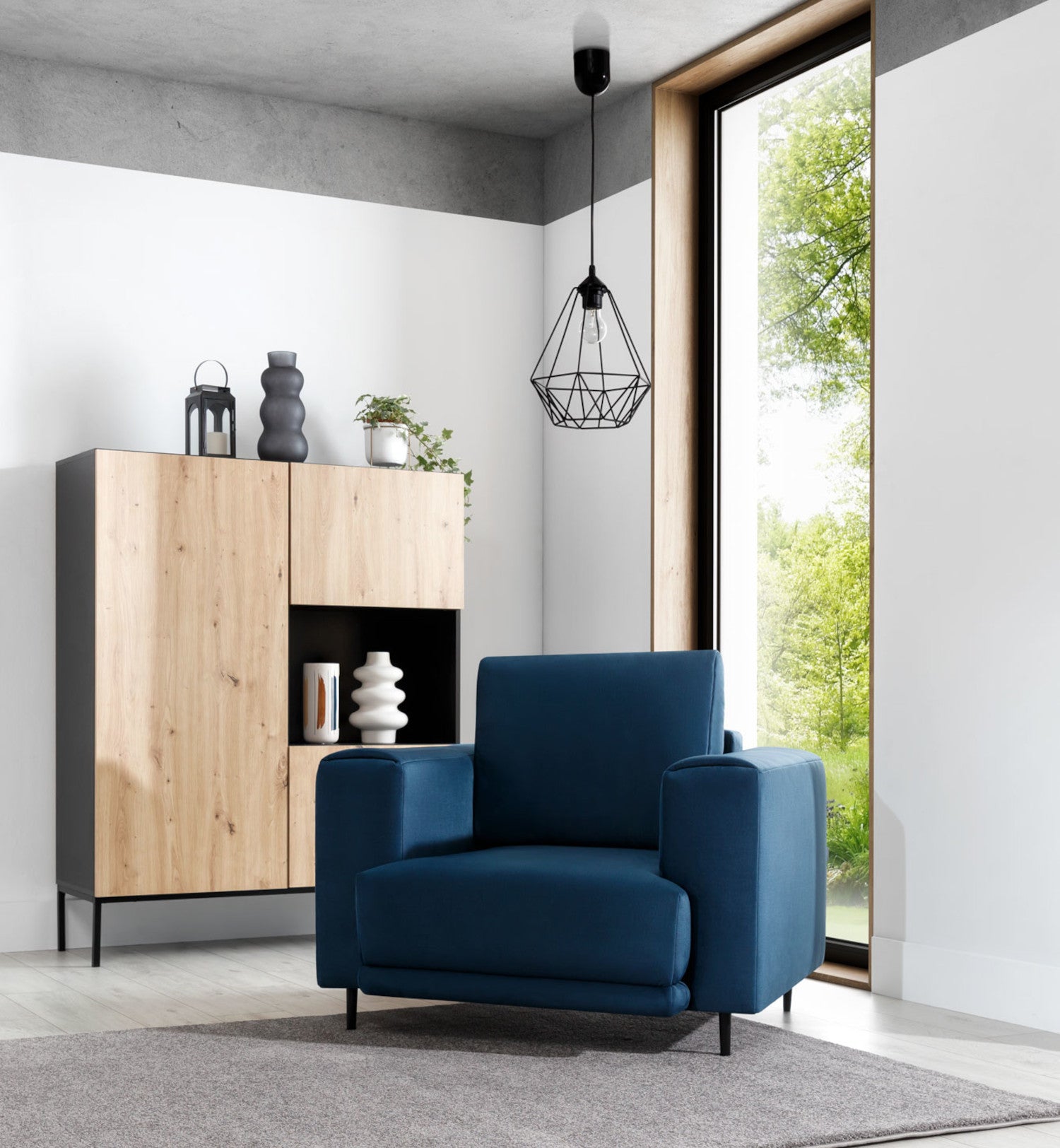 Lampa Benigne 25x90 cm – aranżacja w salonie – nowoczesna lampa loftowa w czarnym kolorze zawieszona nad stolikiem kawowym obok fotela w granatowym odcieniu.