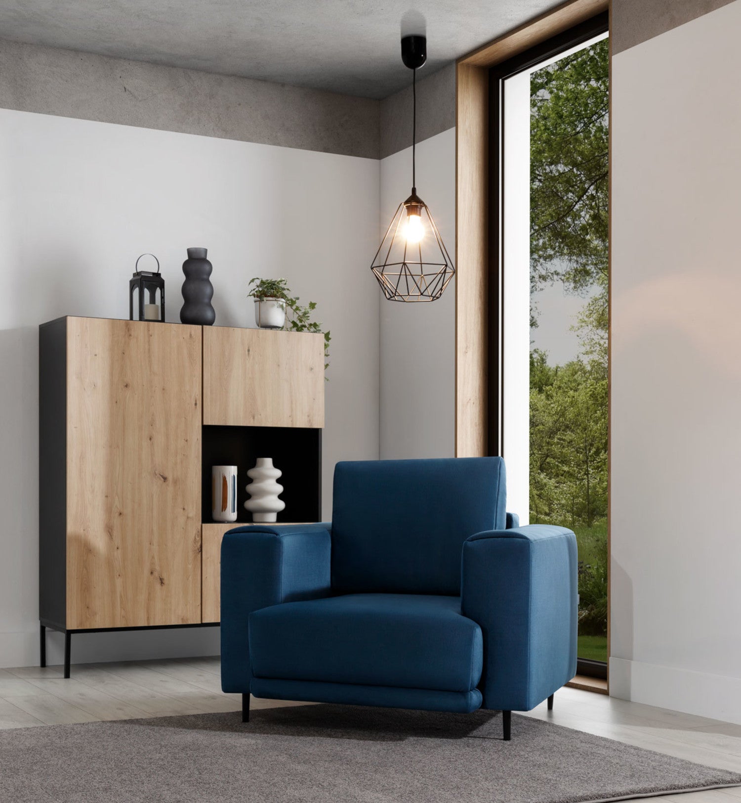 Lampa Benigne 25x90 cm – aranżacja we wnętrzu z oświetleniem – lampa wisząca w stylu industrialnym z zapaloną żarówką, oświetlająca nowoczesny salon z drewnianą komodą i dużym oknem.