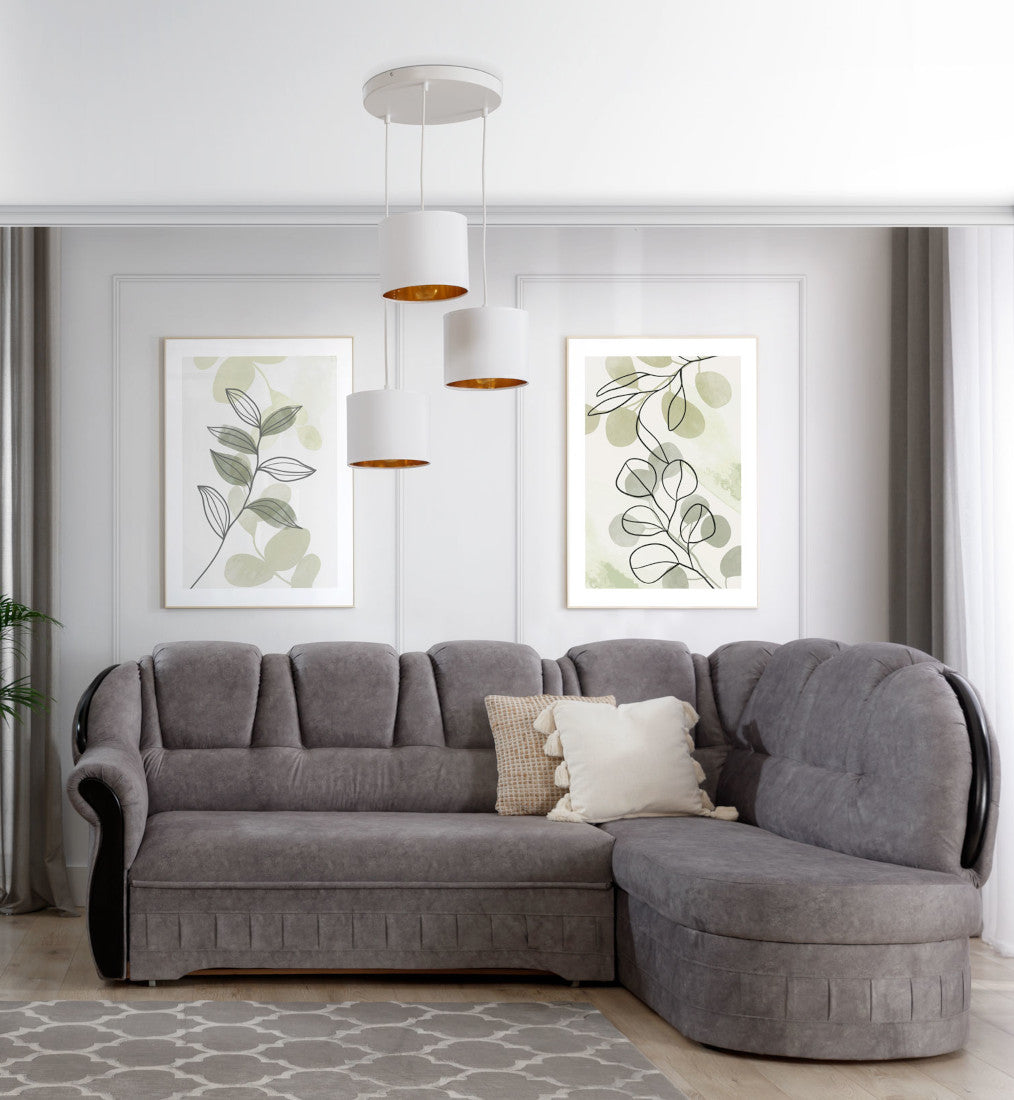 Lampa wisząca Vespillo 3 nad szarą narożną sofą w jasnym salonie z dekoracyjnymi ramami na ścianie i dużym oknem, emitująca dzienne światło przez złote wnętrza abażurów.