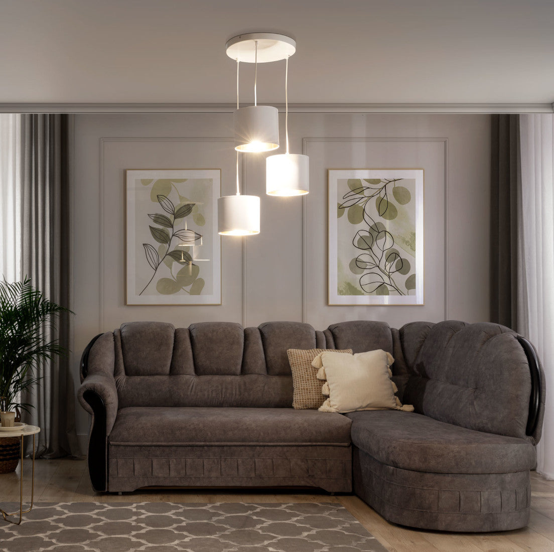 Włączona lampa wisząca Vespillo 3 rzucająca ciepłe, złote światło na szarą sofę i błękitne grafiki na ścianie, w wieczornej aranżacji salonu.