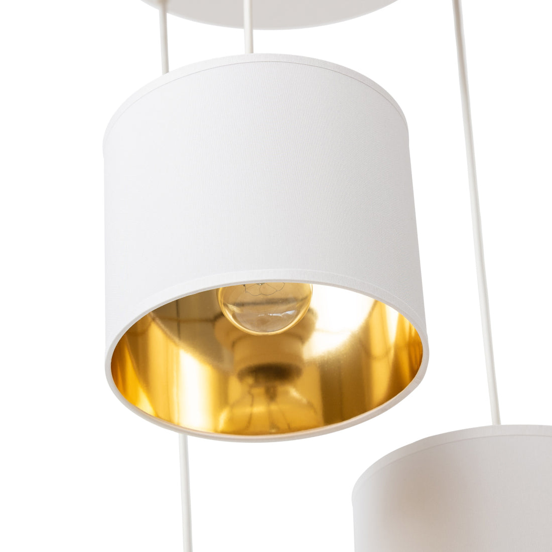 Zbliżenie na biały, cylindryczny abażur lampy Vespillo 3, pokazujące gładką tkaninę i metalowe wsporniki oraz lustrzane, złote wnętrze z widoczną żarówką.