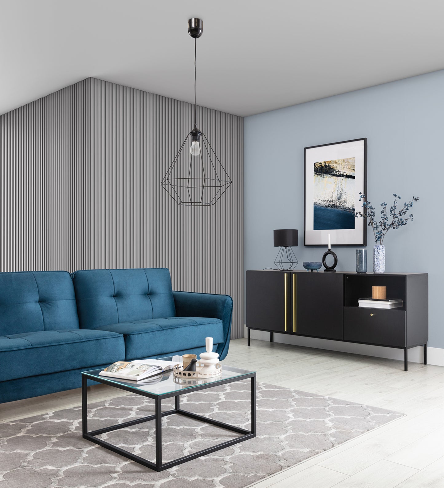 Lampa wisząca Brevitas I 35x90 cm – aranżacja w salonie – czarna lampa loftowa zawieszona na suficie nad stolikiem kawowym w eleganckim wnętrzu z niebieską sofą i czarną komodą.