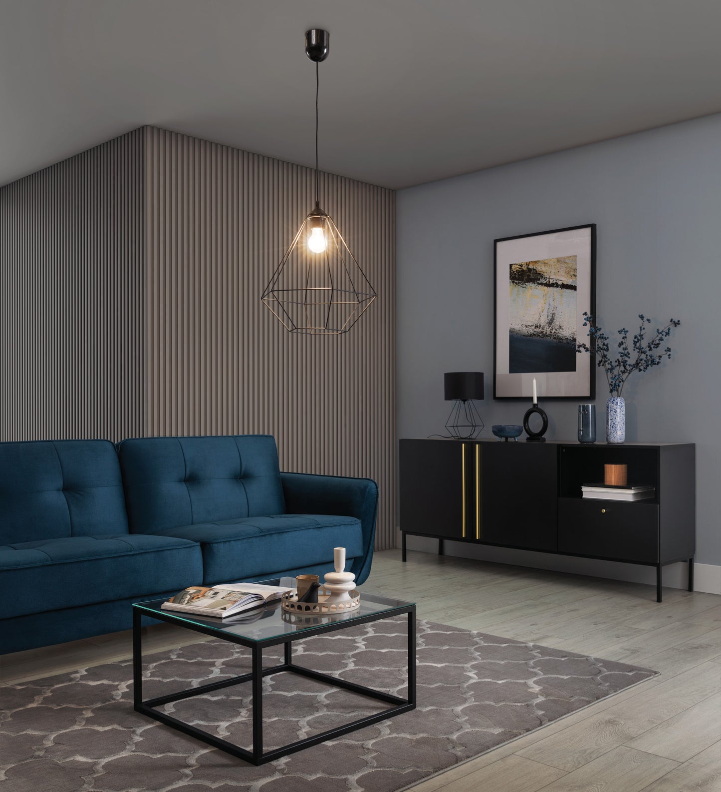 Lampa wisząca Brevitas I 35x90 cm – aranżacja w salonie z oświetleniem – loftowa lampa z zapaloną żarówką, oświetlająca nowoczesny pokój dzienny z szarą ścianą i eleganckimi dodatkami.