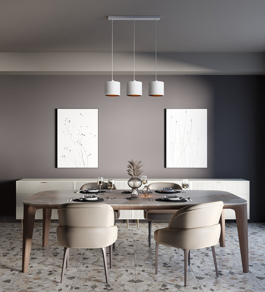 Lampa wisząca liniowa Vespillo 3 nad stołem jadalnianym w eleganckim wnętrzu: trzy abażury równomiernie rozłożone nad drewnianym blatem, na tle ciemnoszarej ściany i sztuki ściennej.