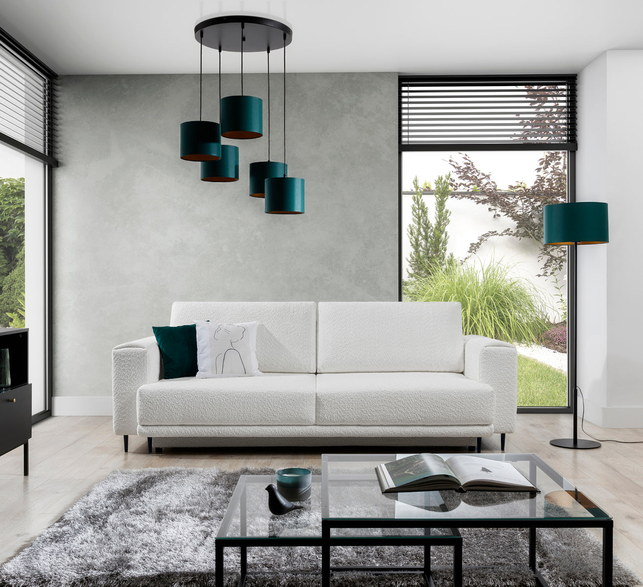 Lampa wisząca Vespillo 5 z pięcioma abażurami zawieszona nad kremową sofą w nowoczesnym salonie z betonową ścianą i dużymi przeszkleniami, emitująca dzienne światło przez zielone klosze.