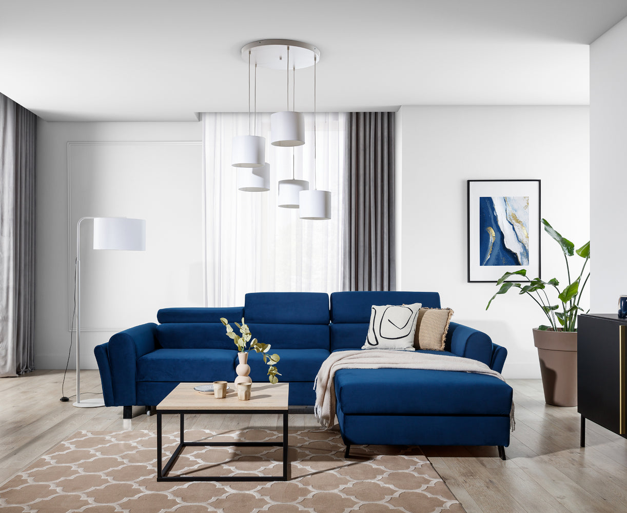 Jasny, nowoczesny salon z granatową sofą i dużymi oknami, nad którym unosi się biała lampa sufitowa Vespillo 5 z pięcioma abażurami.