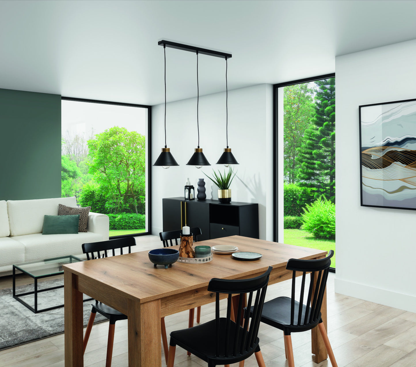 Nowoczesne wnętrze jadalni i salonu w świetle dziennym, z drewnianym stołem i czterema krzesłami, nad którymi zwisa czarna lampa Detmer 3 nad czarną komodą i białym fotelem przy dużym oknie.