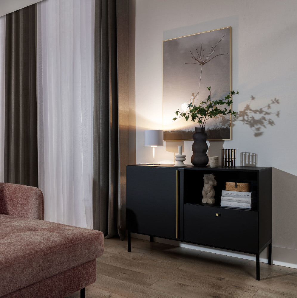 Włączona lampka nocna Vespillo rzucająca ciepłe, złote światło na półkę z dekoracjami i zasłony, w przytulnej wieczornej aranżacji salonu.