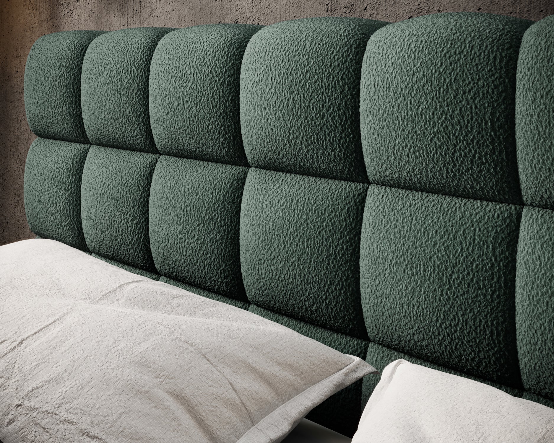 Tapicerowany zagłówek łóżka Magentta w ciemnozielonej tkaninie o wypukłych, miękkich przeszyciach, na tle betonowej ściany.