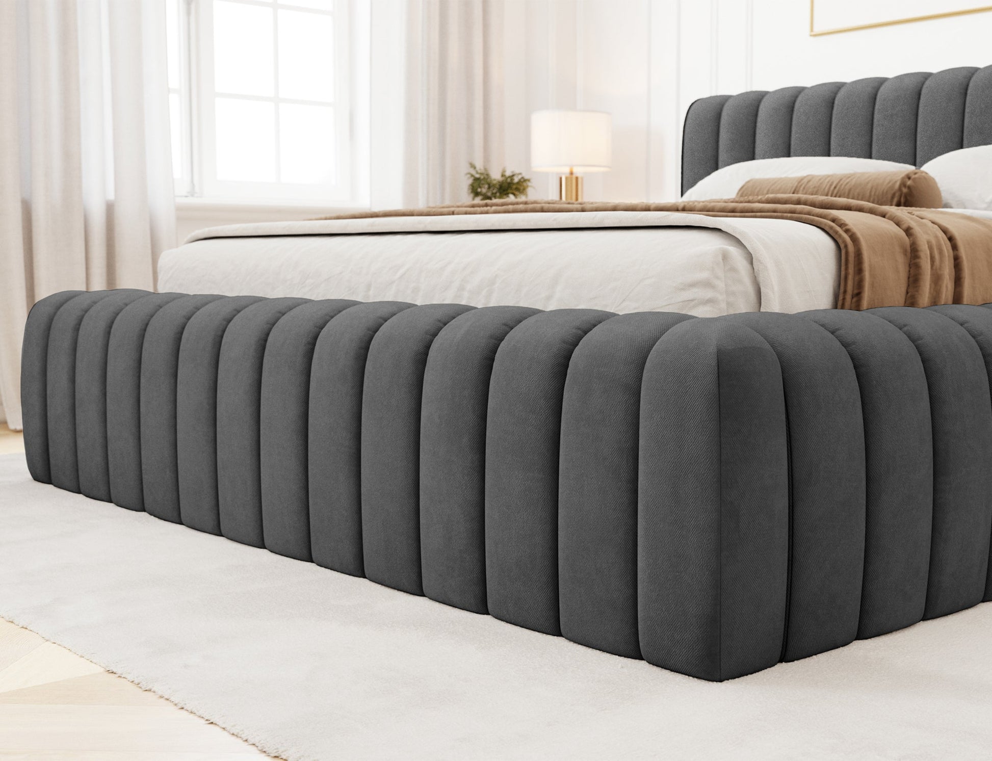 Zbliżenie na dolną część ramy łóżka Carilla w tkaninie Sola 06 ciemnoszary, tapicerowane pionowymi panelami.