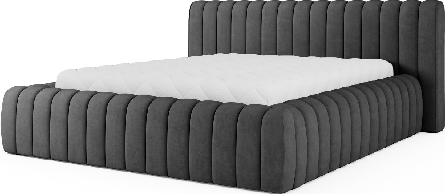 Ciemnoszare łóżko tapicerowane Carilla Sola 06 z pionowymi przeszyciami i materacem, widok z ukosa na białym tle.