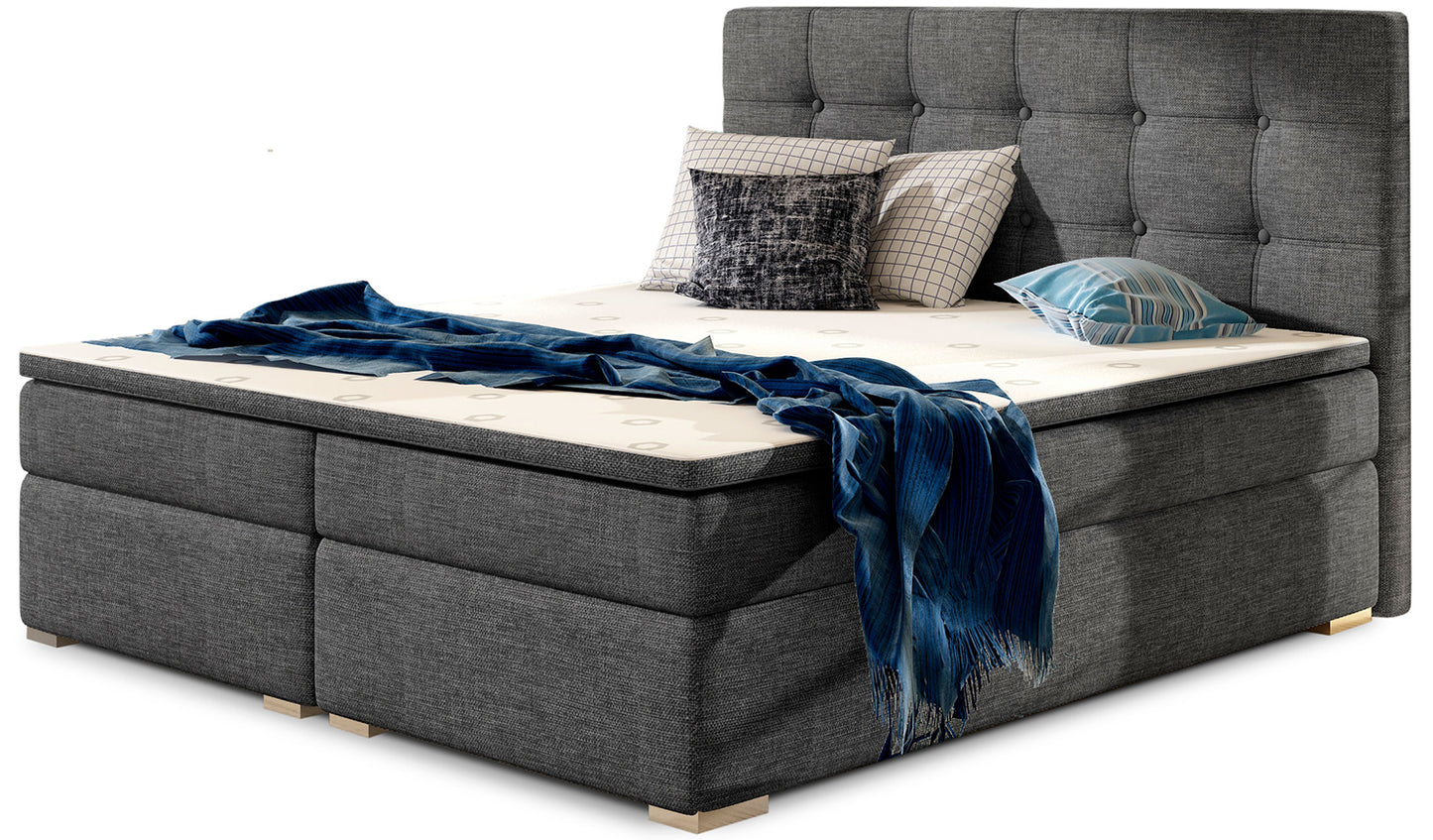 Łóżko kontynentalne Inez 180x200 cm w kolorze Sawana 05 ciemnoszary, z wysokim tapicerowanym zagłówkiem pikowanym w kwadraty.