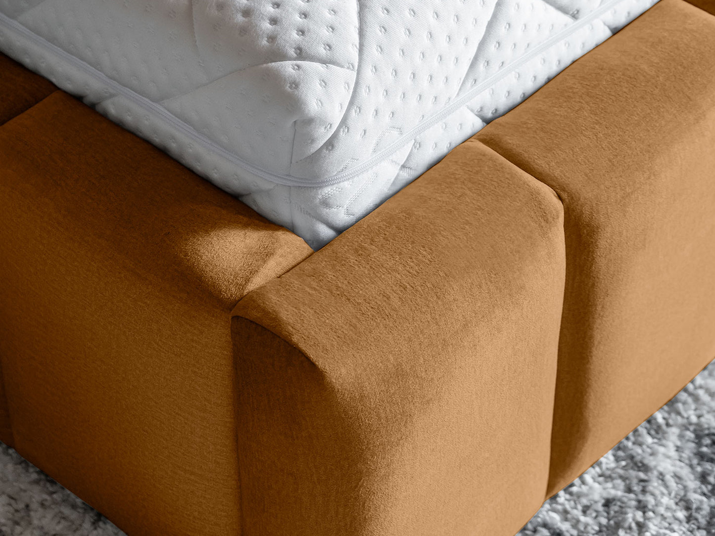 Detal narożnika materaca opierającego się na ramie łóżka Lamica Monolith 48 miodowy (140 × 200 cm), uwypuklający kontrast białego materaca z aksamitnym welurem.