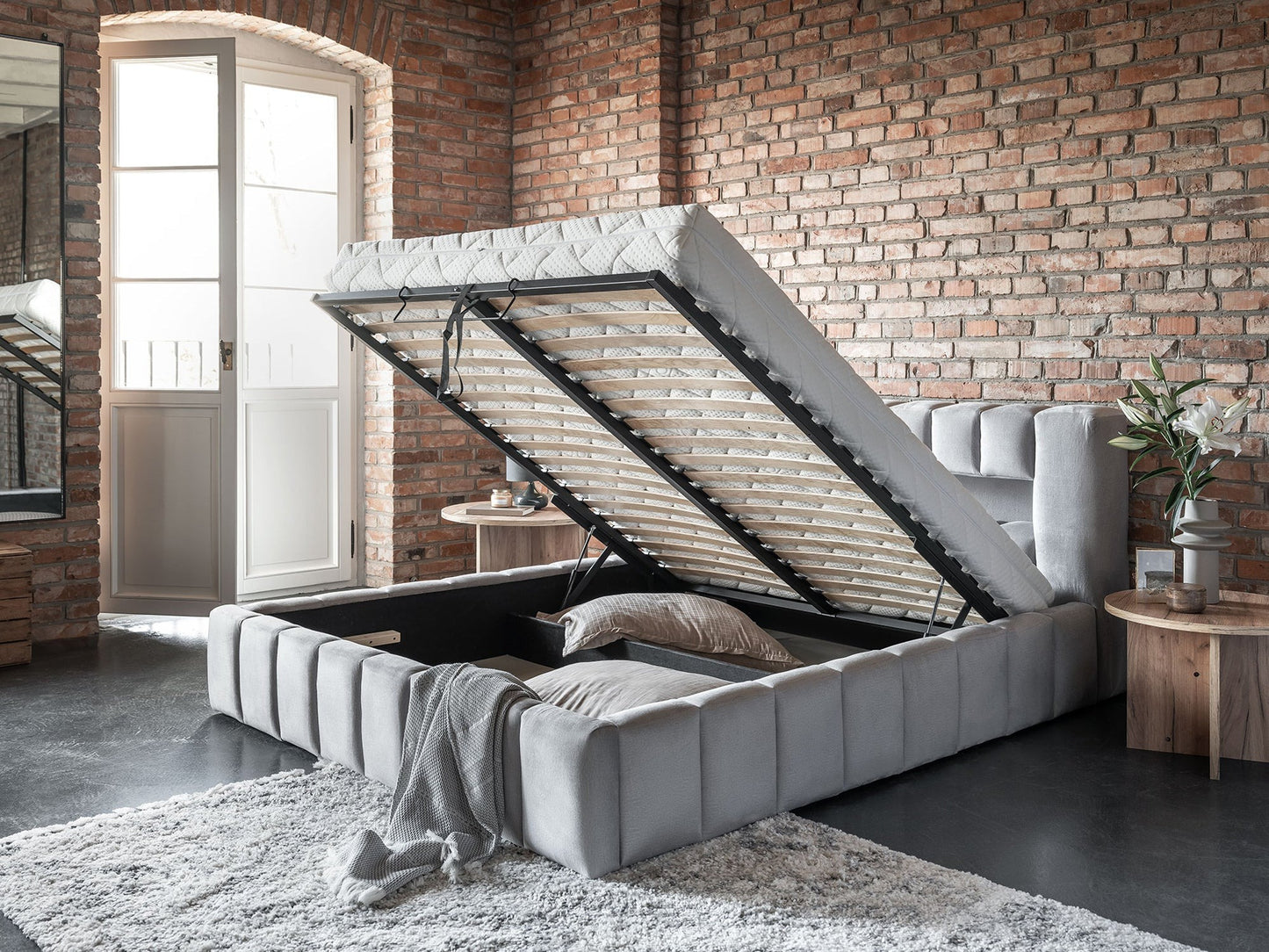 Uniesiony stelaż łóżka Lamica Monolith 84 jasnoszary (140×200 cm) odsłaniający pojemną, tapicerowaną skrzynię do przechowywania.